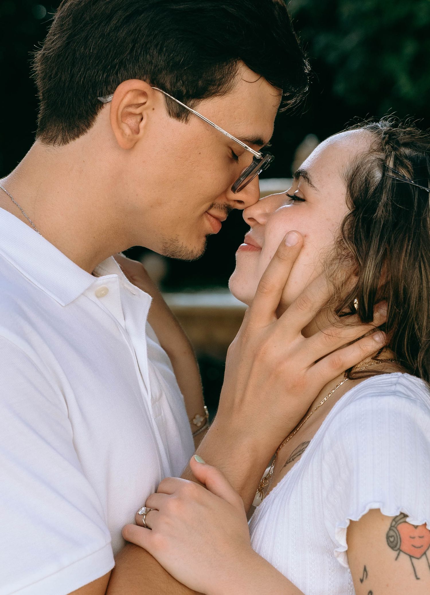 A young couple in white outfits share a romantic moment, nearly kissing while smiling at each other outdoors. Engagement photos on Worth Ave