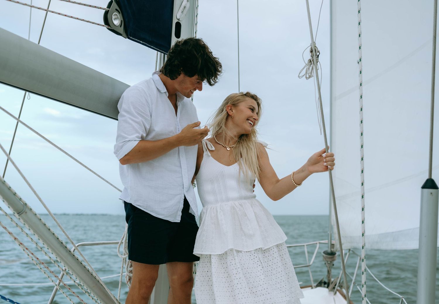 Couple laughing and enjoying a romantic sailing trip on a yacht on a cloudy day.