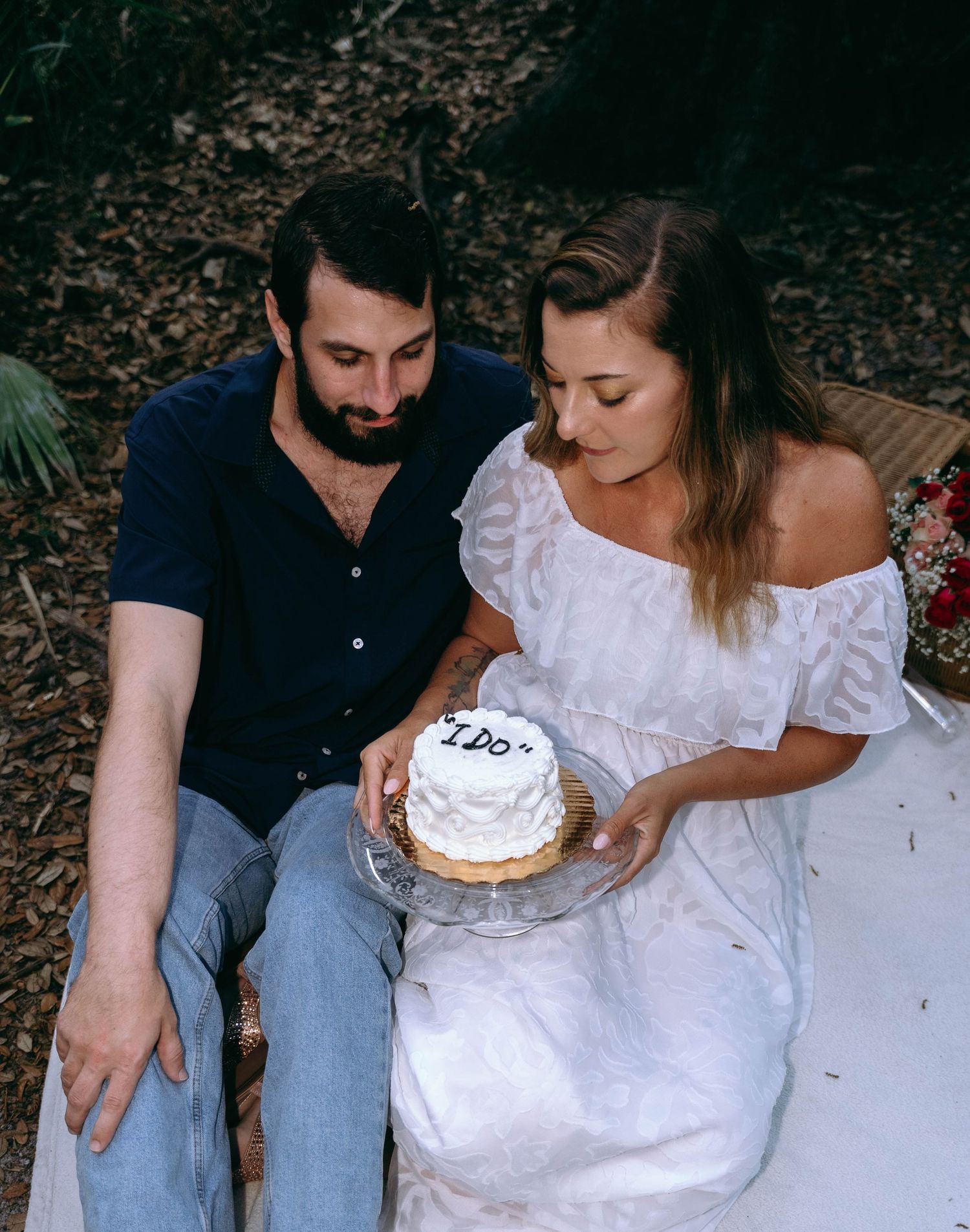 A couple sits together on the ground sharing a small white cake.