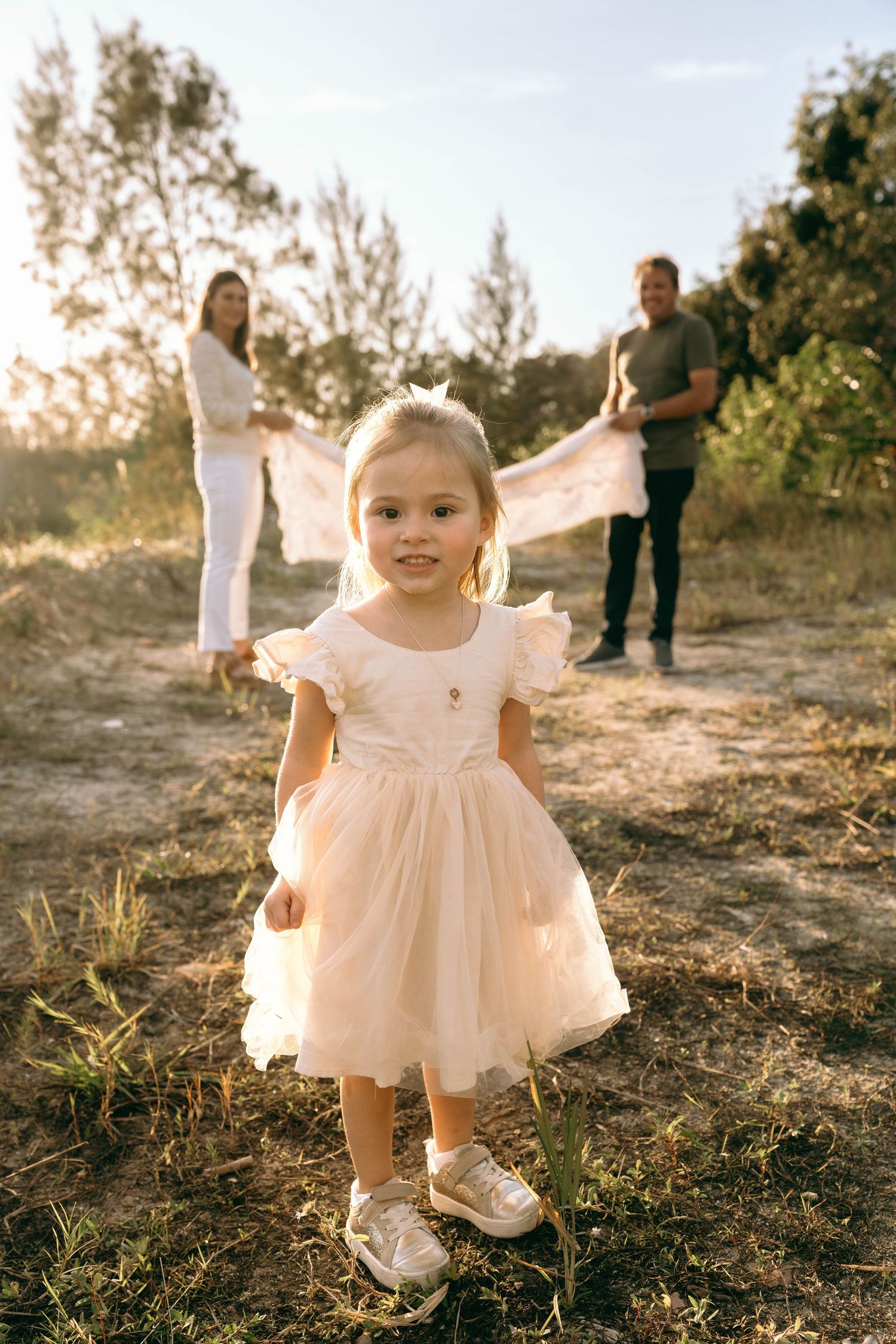 Little girl in a white dress twirling during an outdoor photoshoot at sunset.