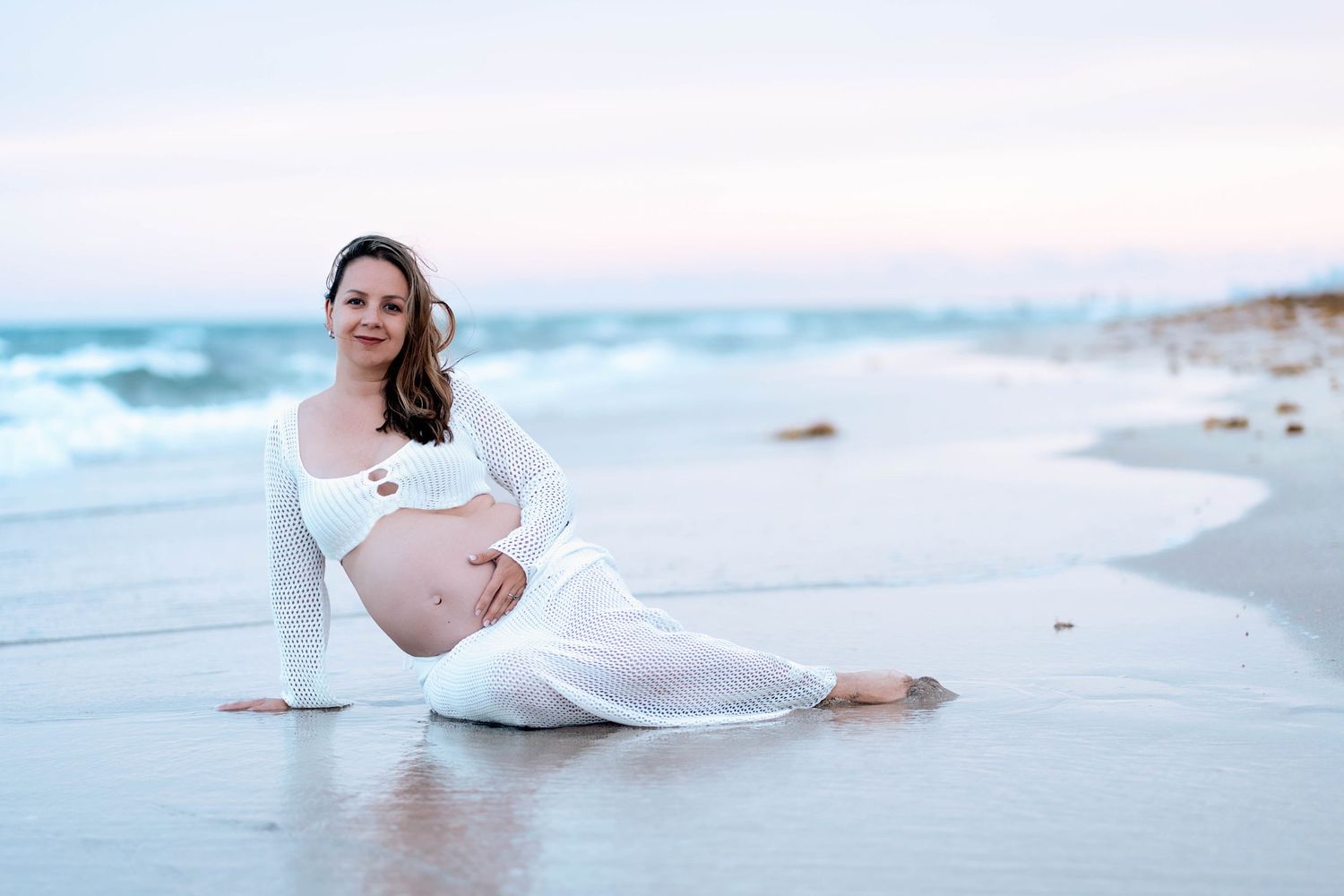 Beachside maternity photos with waves and soft lighting.
