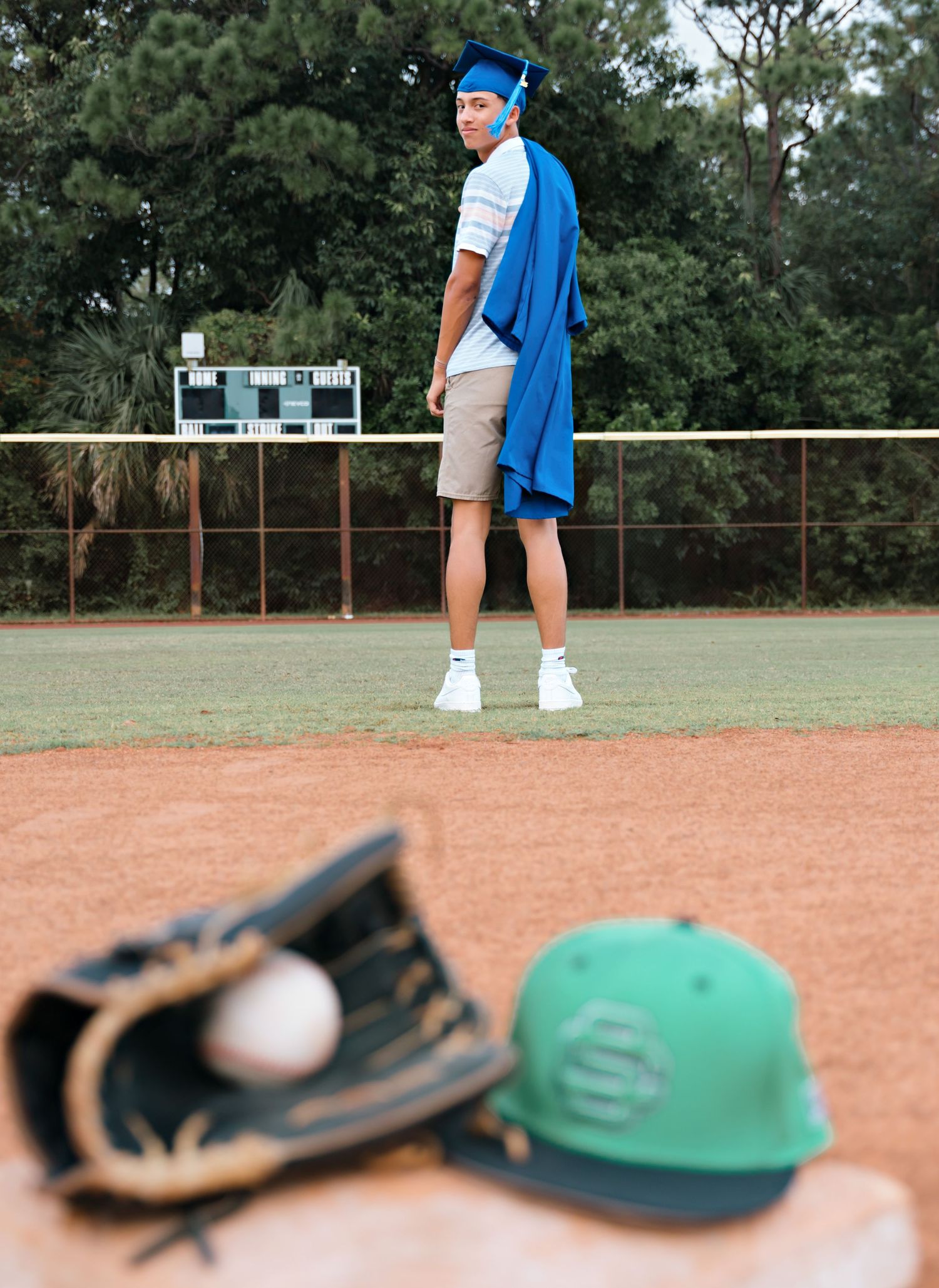 Baseball-themed photo with glove and cap on dirt field with player in background.