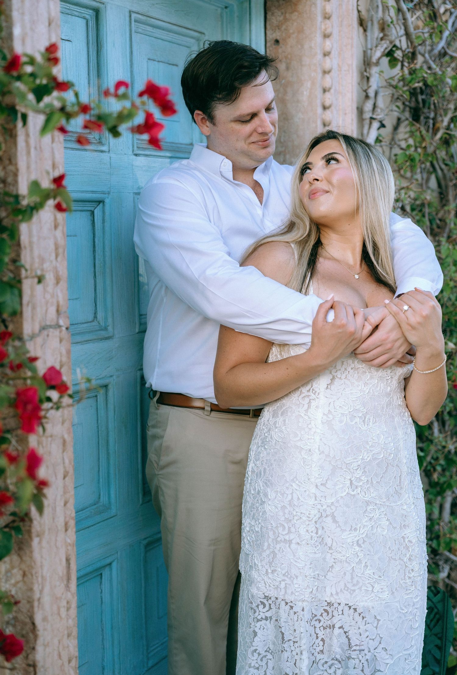 Couple embracing tenderly by a rustic blue door adorned with red climbing roses.