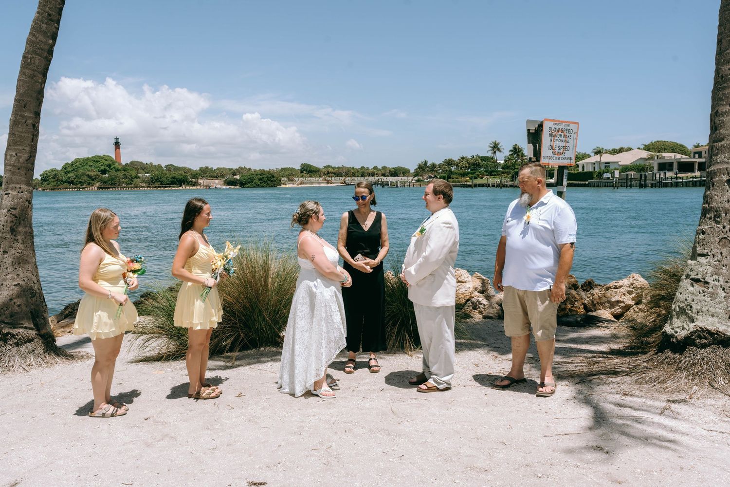 Small wedding ceremony on a sunny Florida waterfront with six people gathered near palm trees and a scenic bay backdrop.