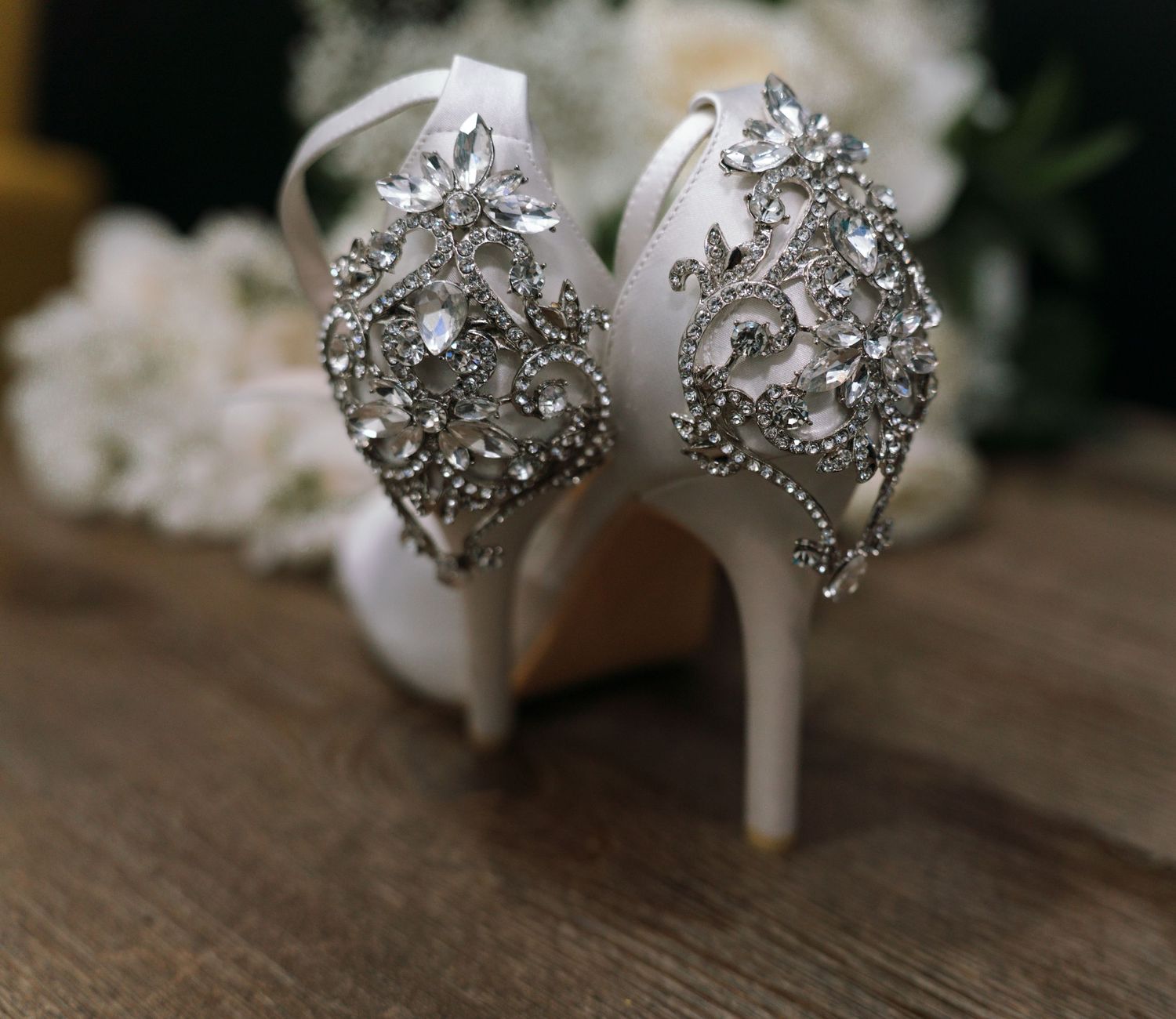 Elegant bridal shoes with ornate crystal embellishments displayed on a wooden surface.