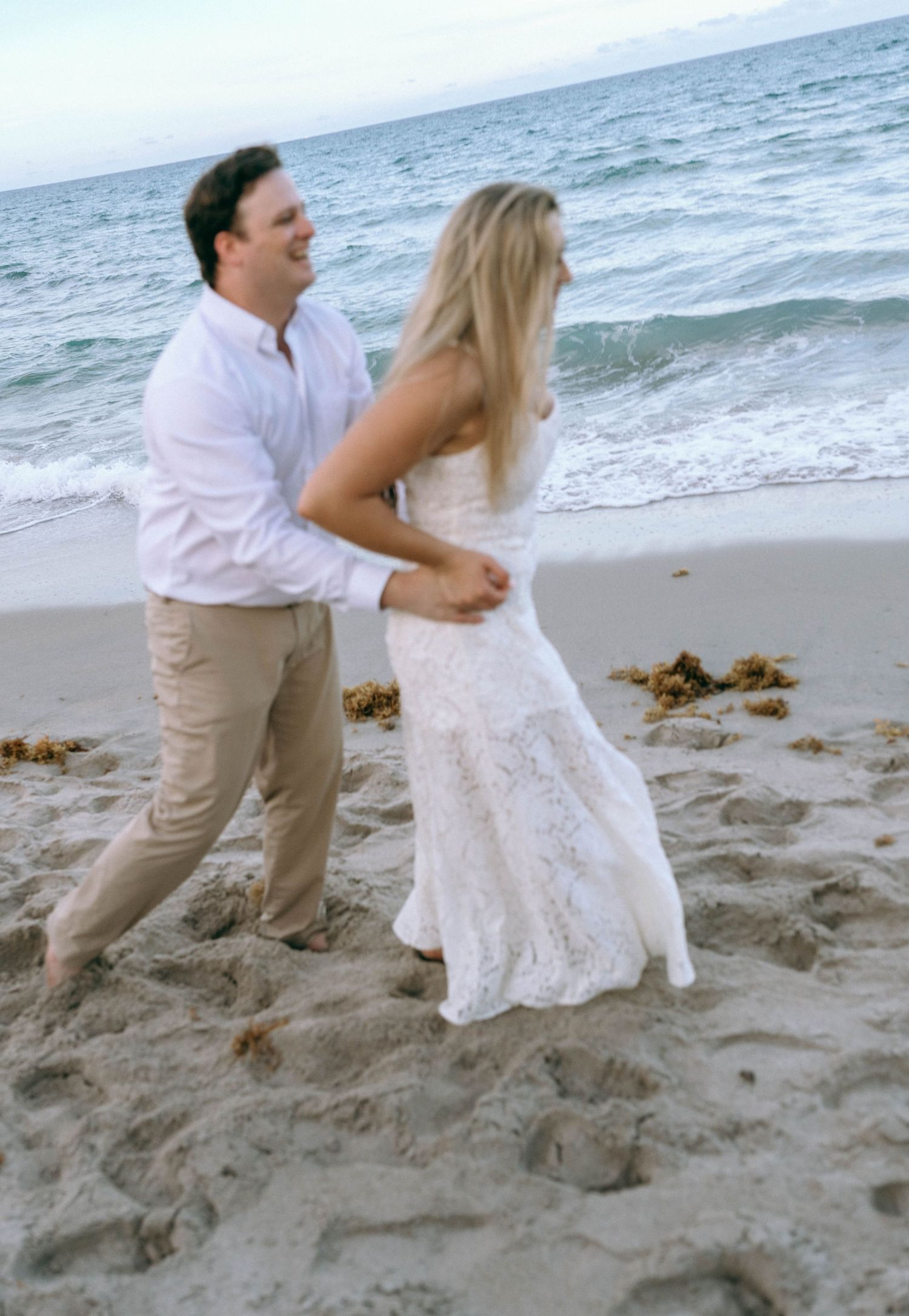 Laughing couple dancing playfully together on a sandy beach by the ocean waves.