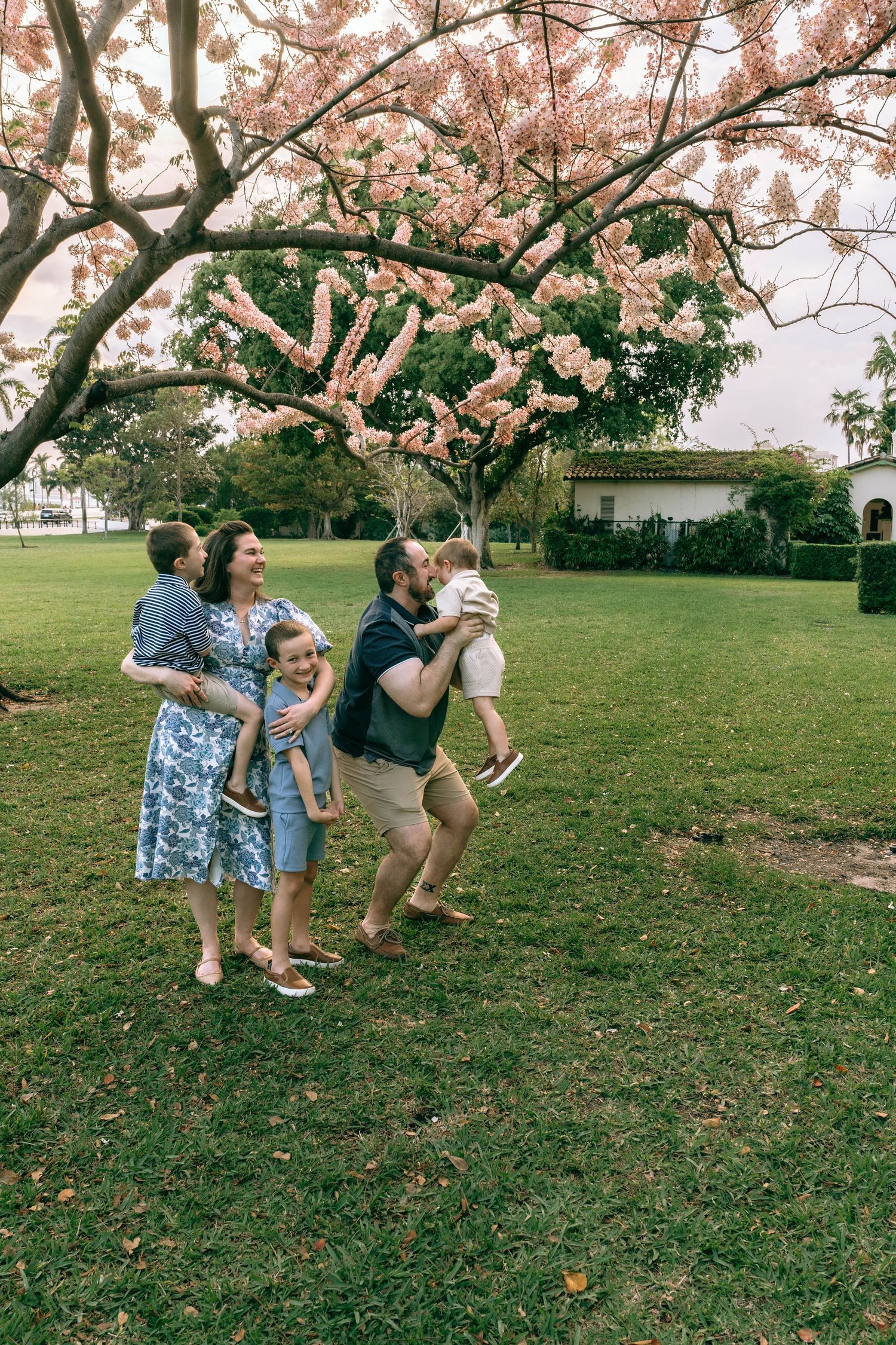 Family of five enjoying a sunny day in a lush green park under a blooming pink flowering tree.  Family photos at Bradley Park Palm Beach, FL