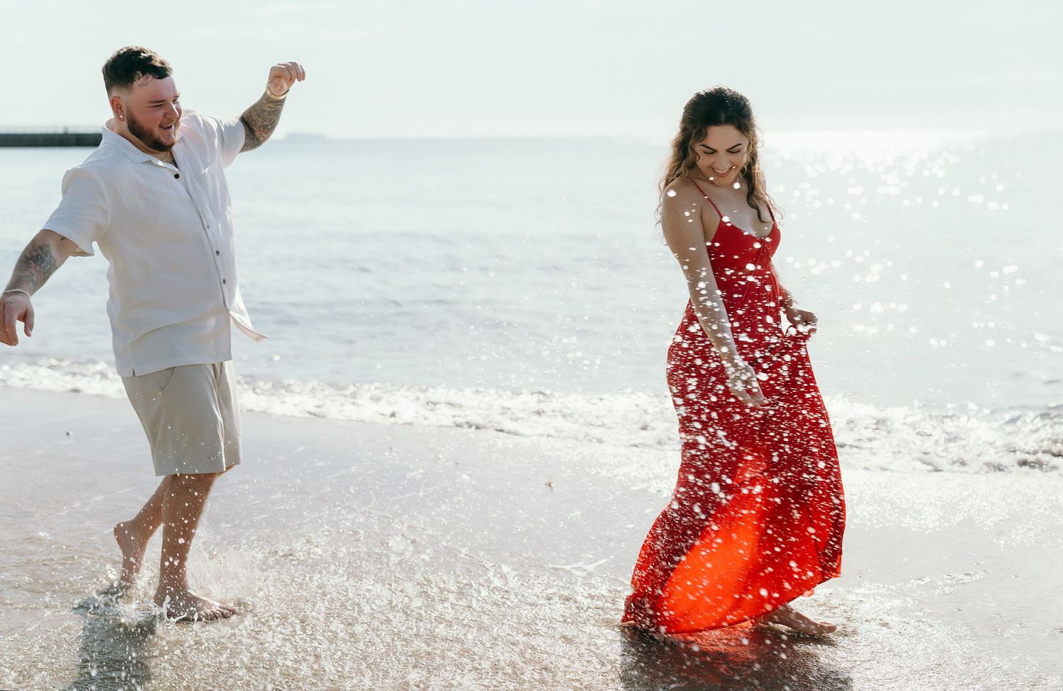 A couple splashes playfully in the ocean waves at sunset.