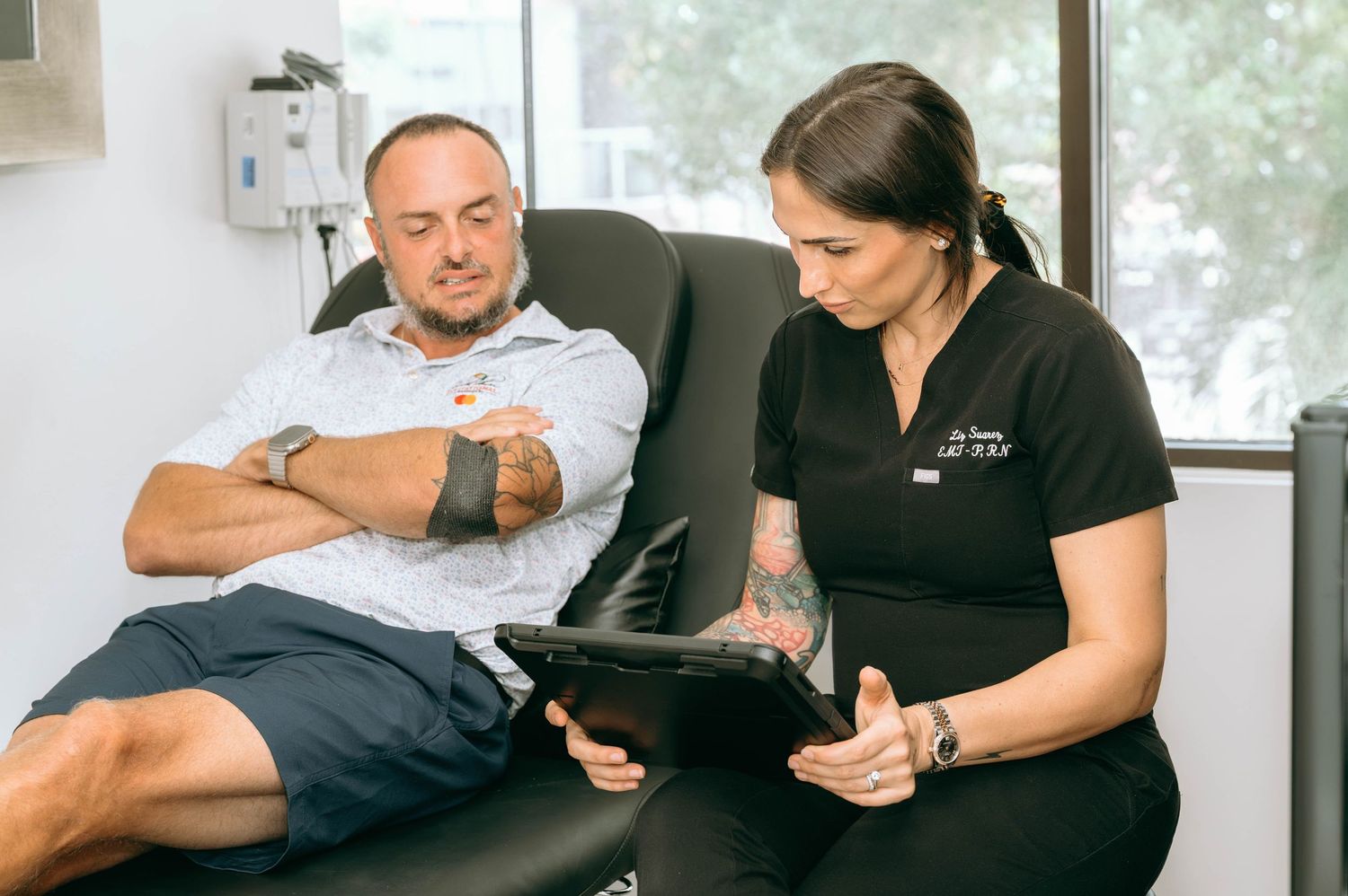 Healthcare professional reviewing tablet with male patient reclining in medical chair during consultation.