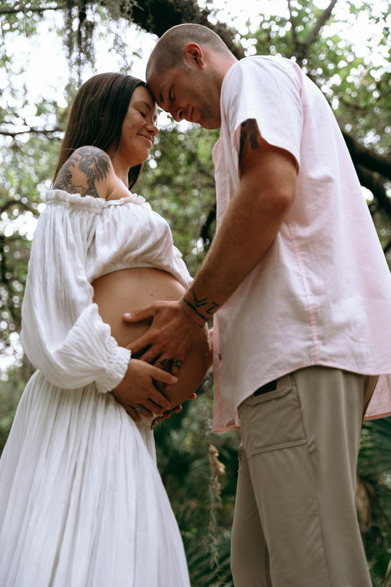 An intimate maternity photo of a couple in white clothing sharing a tender moment.