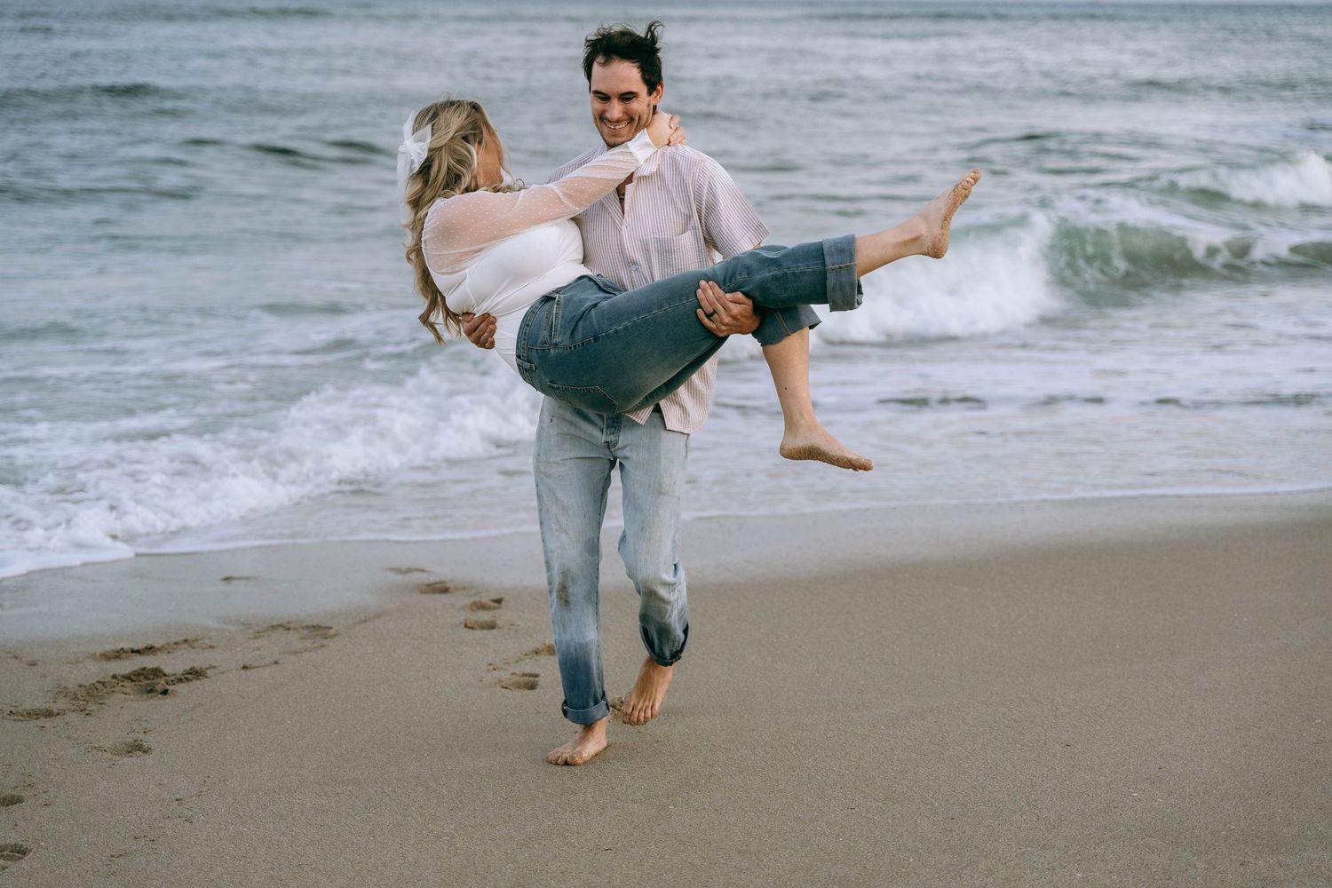 A playful couple dances and spins on the beach with ocean waves in the background.