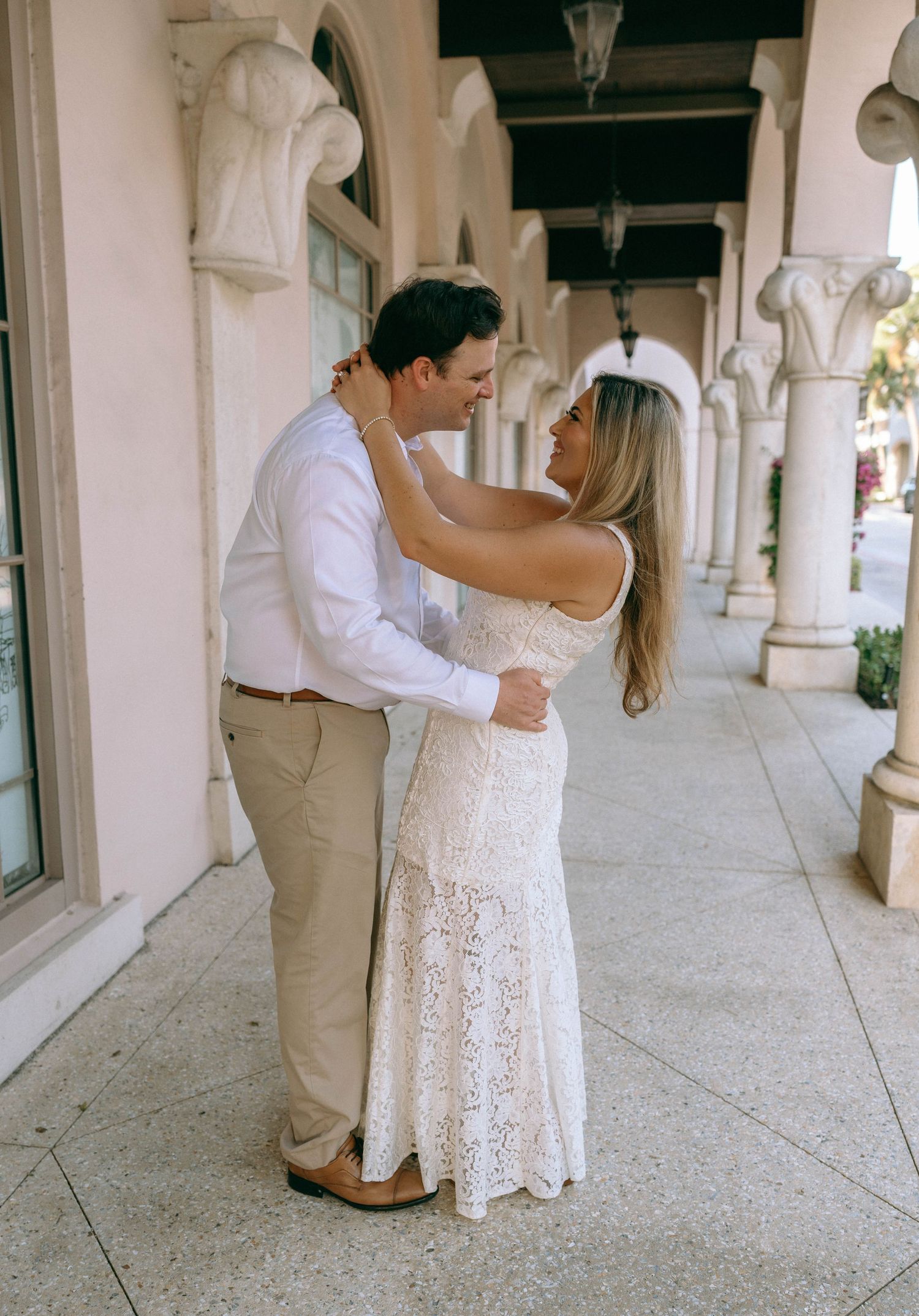 Elegant couple embracing under arched columns in a classic architectural setting.
