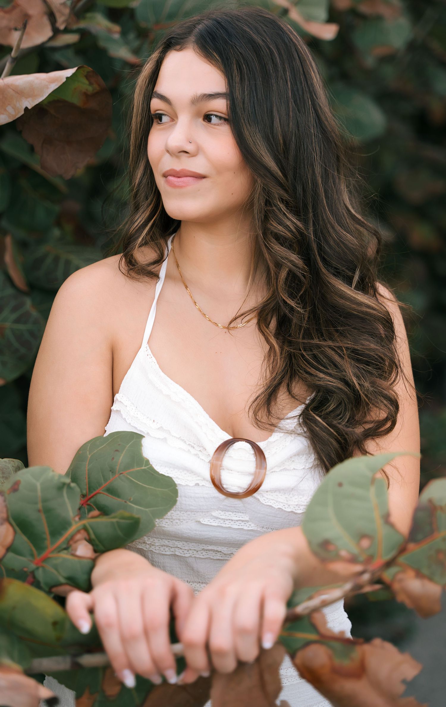 Fashion portrait with white camisole among green foliage in natural setting.
