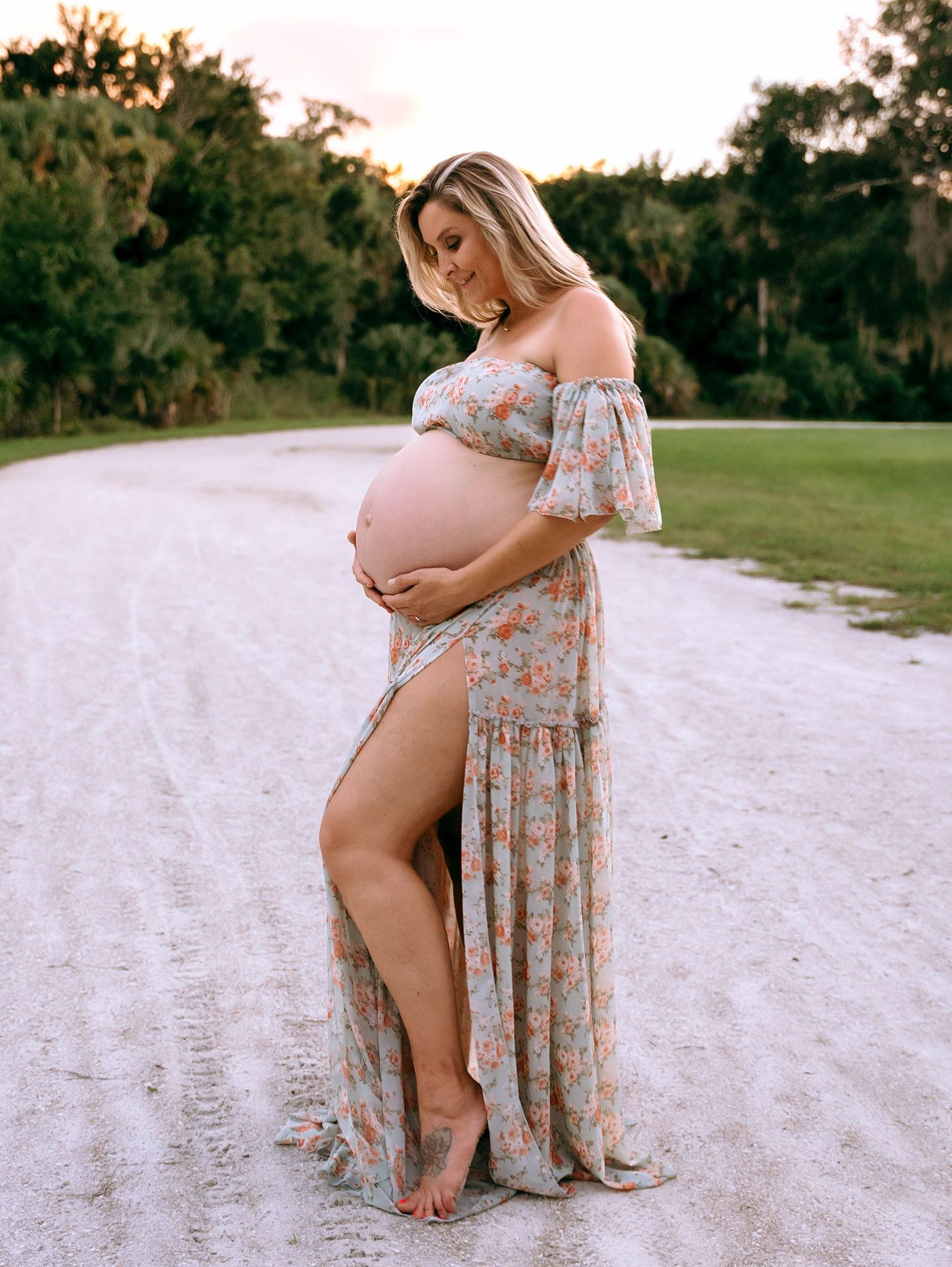 A floral maternity dress creates elegant silhouettes against a sandy beach backdrop.