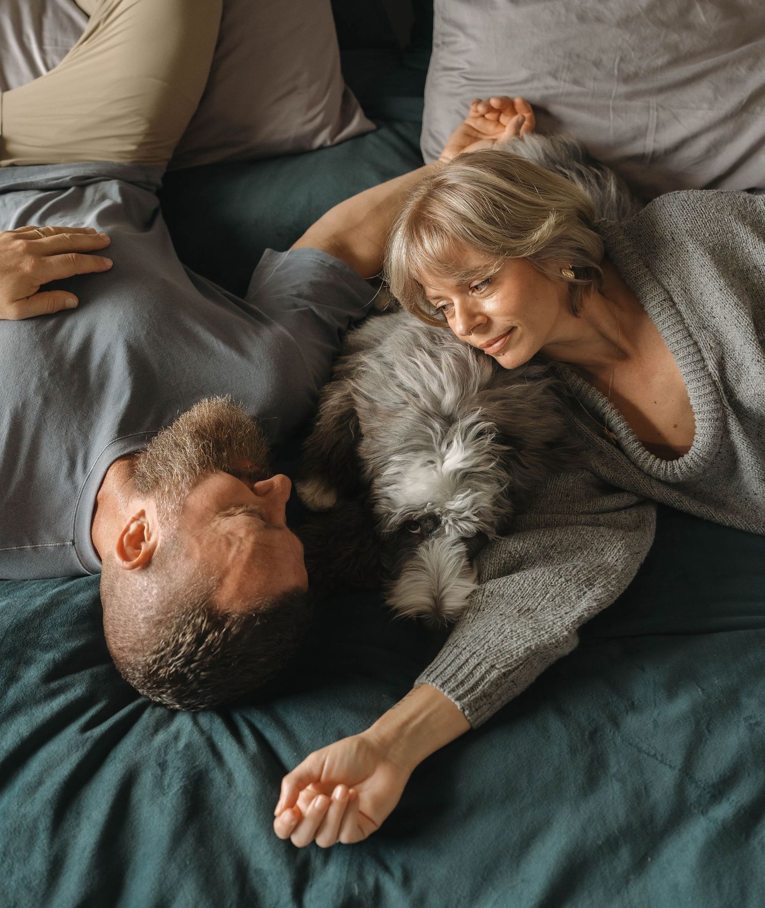 A couple and their fluffy pet dog relax together on cozy bedding.