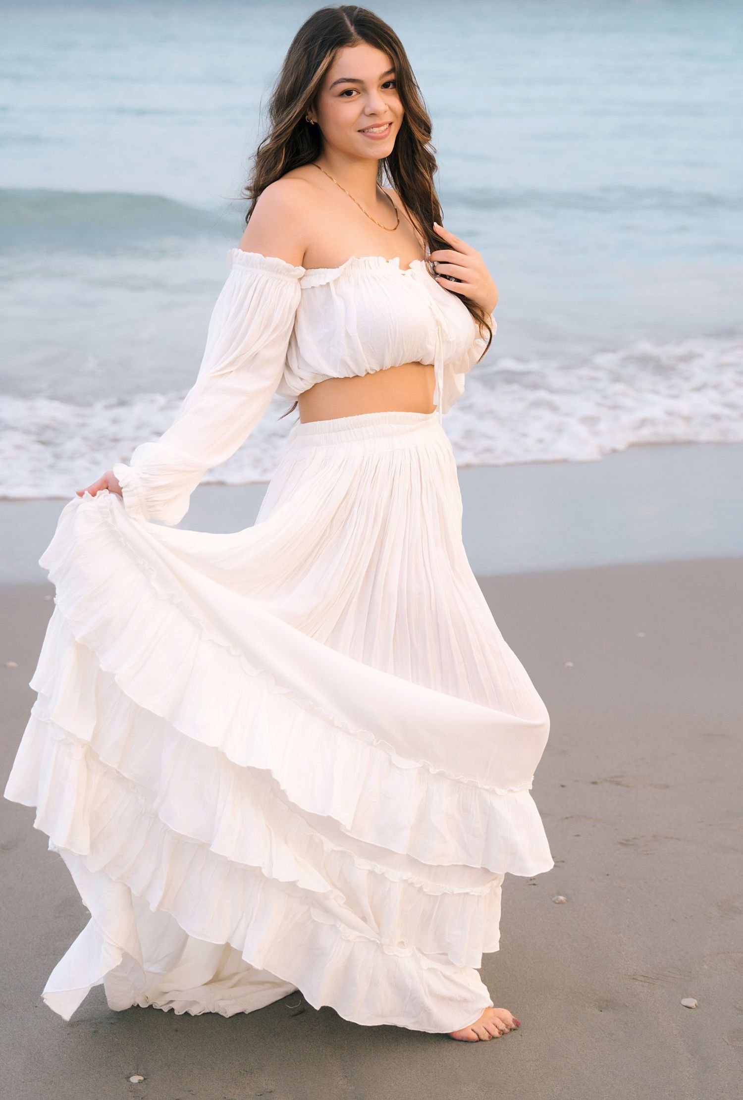 Flowing white maxi dress twirls during sunset beach photography session.