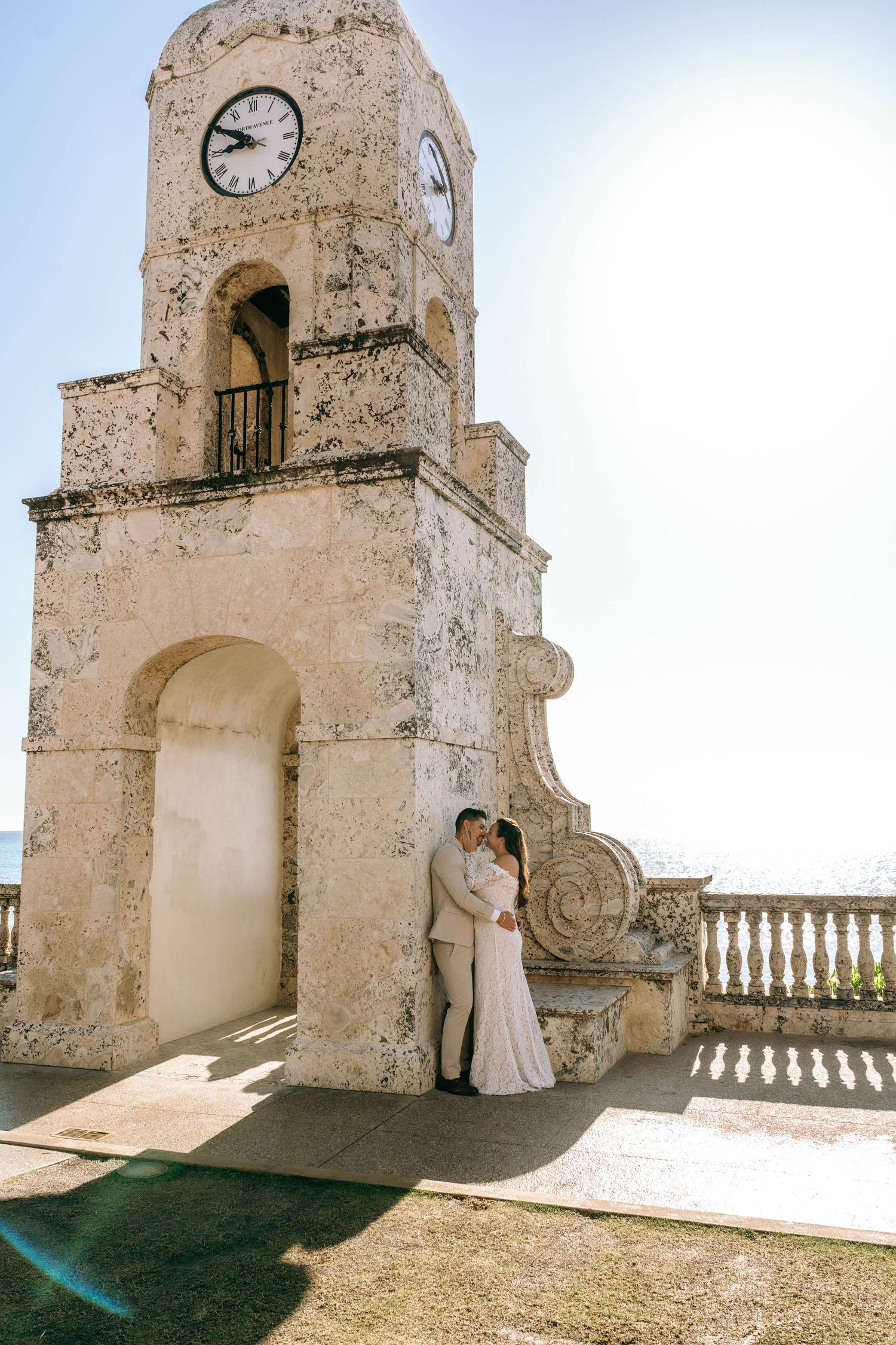 Bride and groom embracing under historic clock tower in Palm Beach, Florida on their wedding day. Worth Avenue, Palm Beach, FL