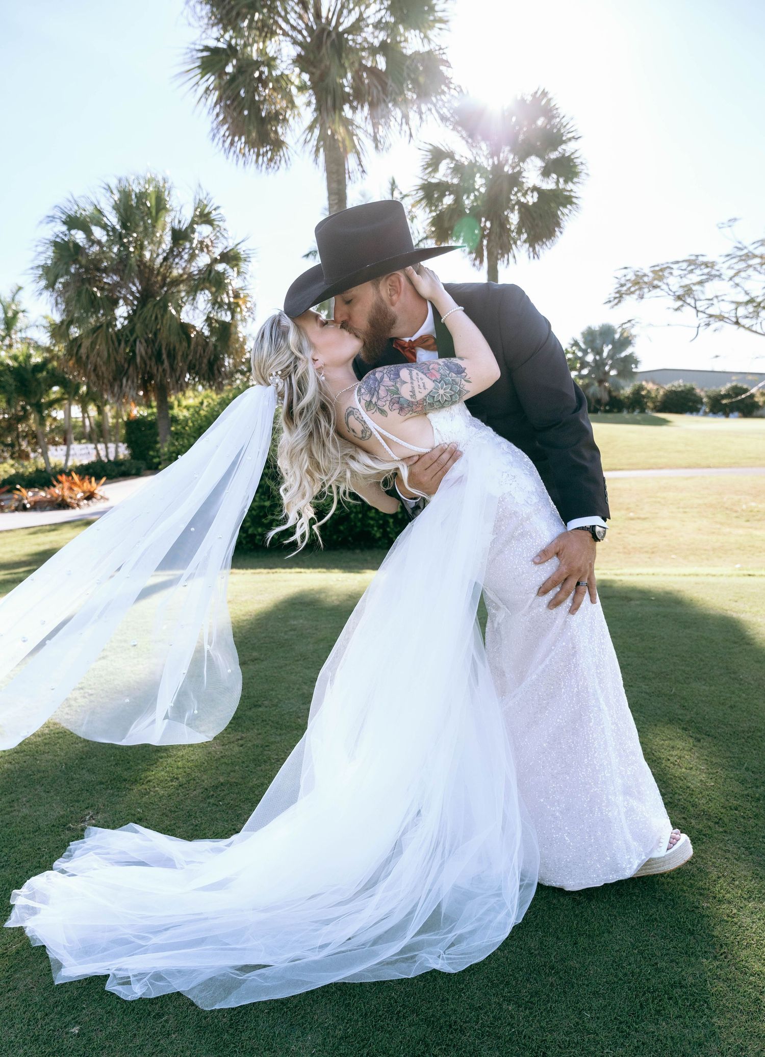 Bride and groom in dramatic pose on grass with flowing white dress and veil.