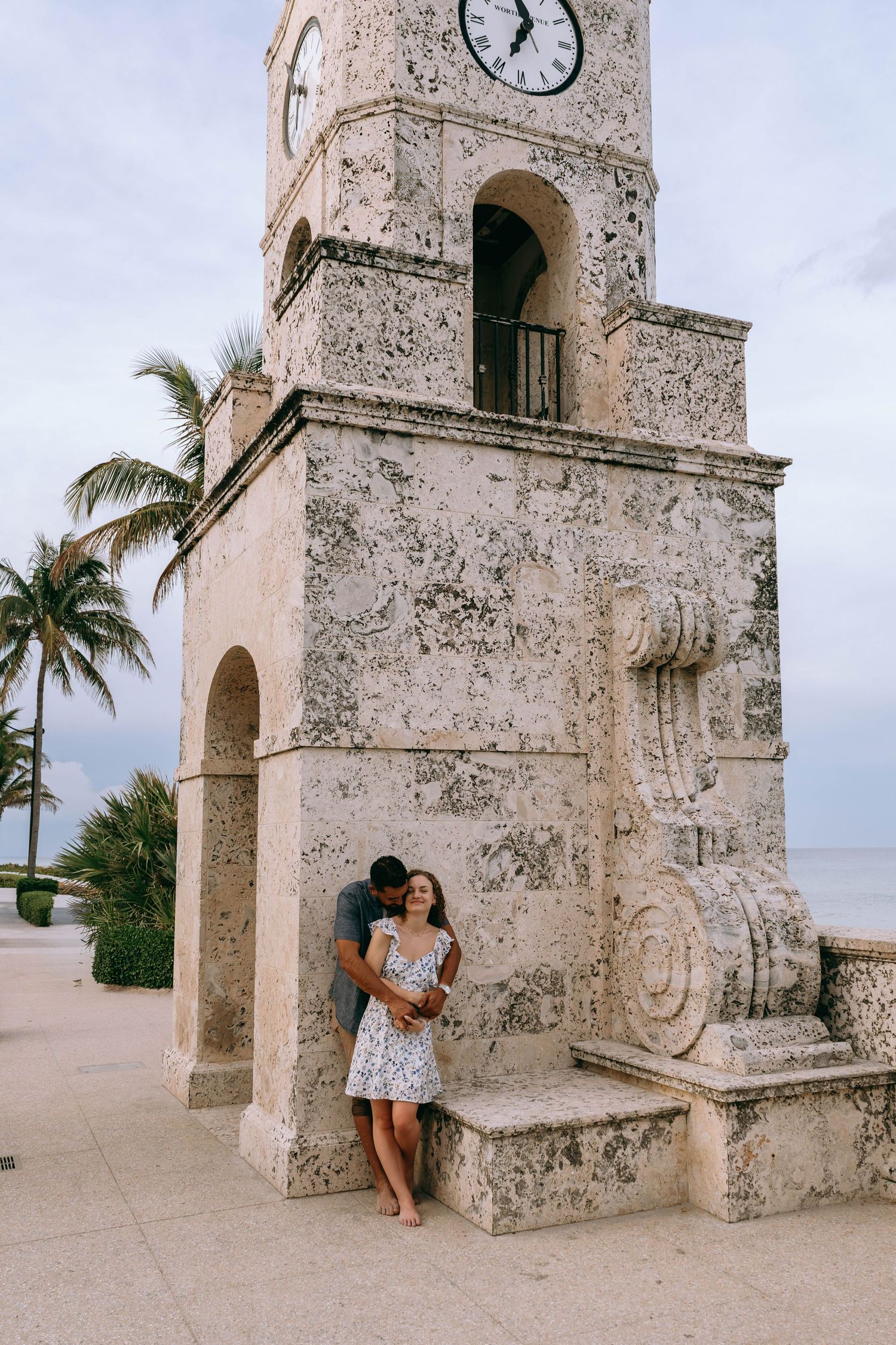 Couple embracing beneath a historic stone clock tower near the beach in Palm Beach, Florida on Worth Avenue Palm beach.