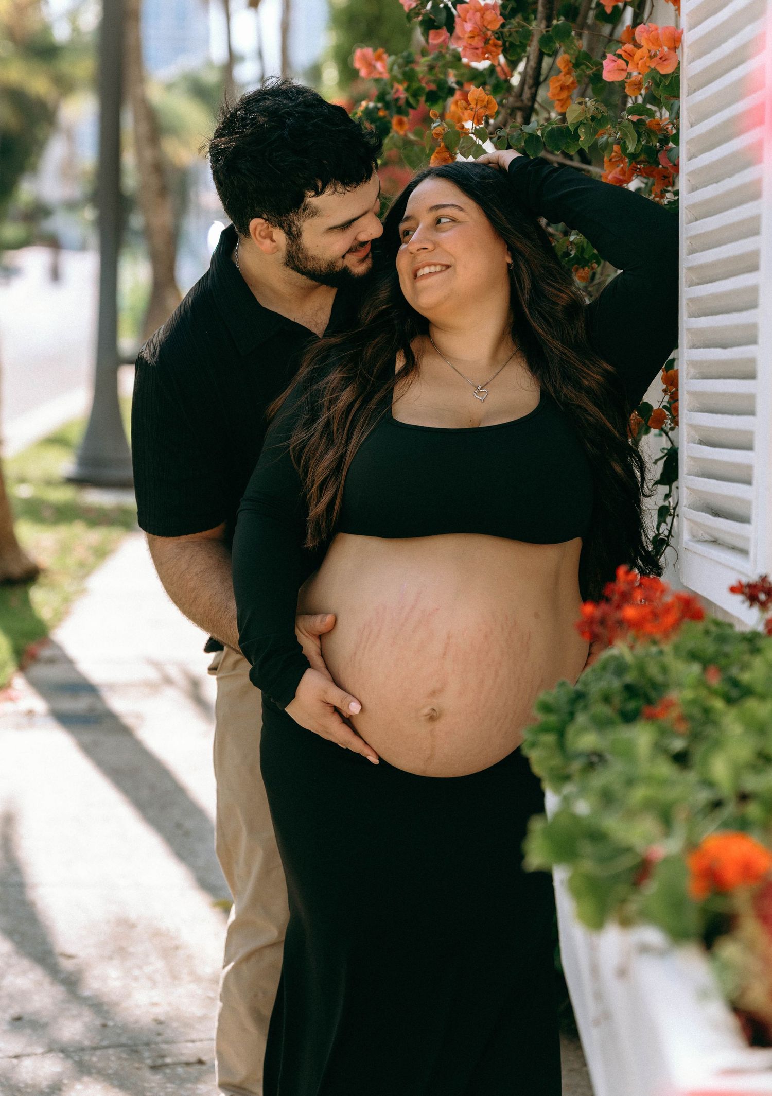 Couple sharing tender maternity moment outdoors with colorful bougainvillea blooms in background. Worth Avenue, Palm Beach, FL