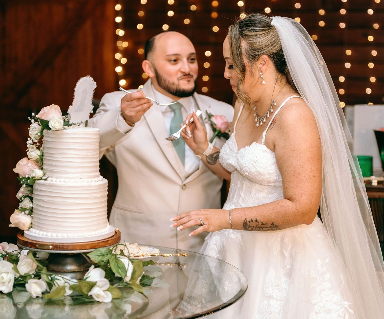 Wedding celebration with elegant white tiered cake decorated with roses and string lights in the background.