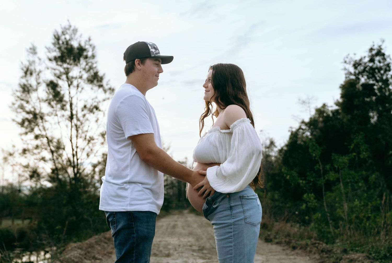 Couple in casual white shirts and jeans share tender moments in a grassy field at sunset.