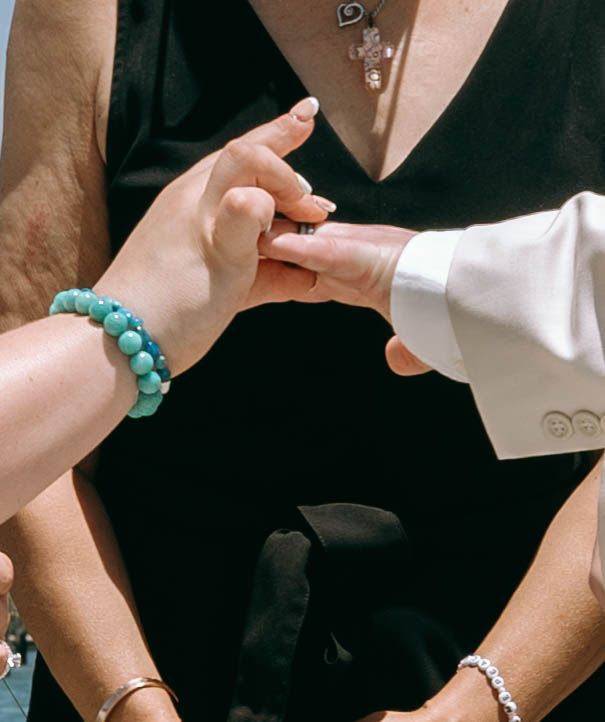 Close-up of hands exchanging a ring, with turquoise beaded bracelet, during an outdoor wedding ceremony.