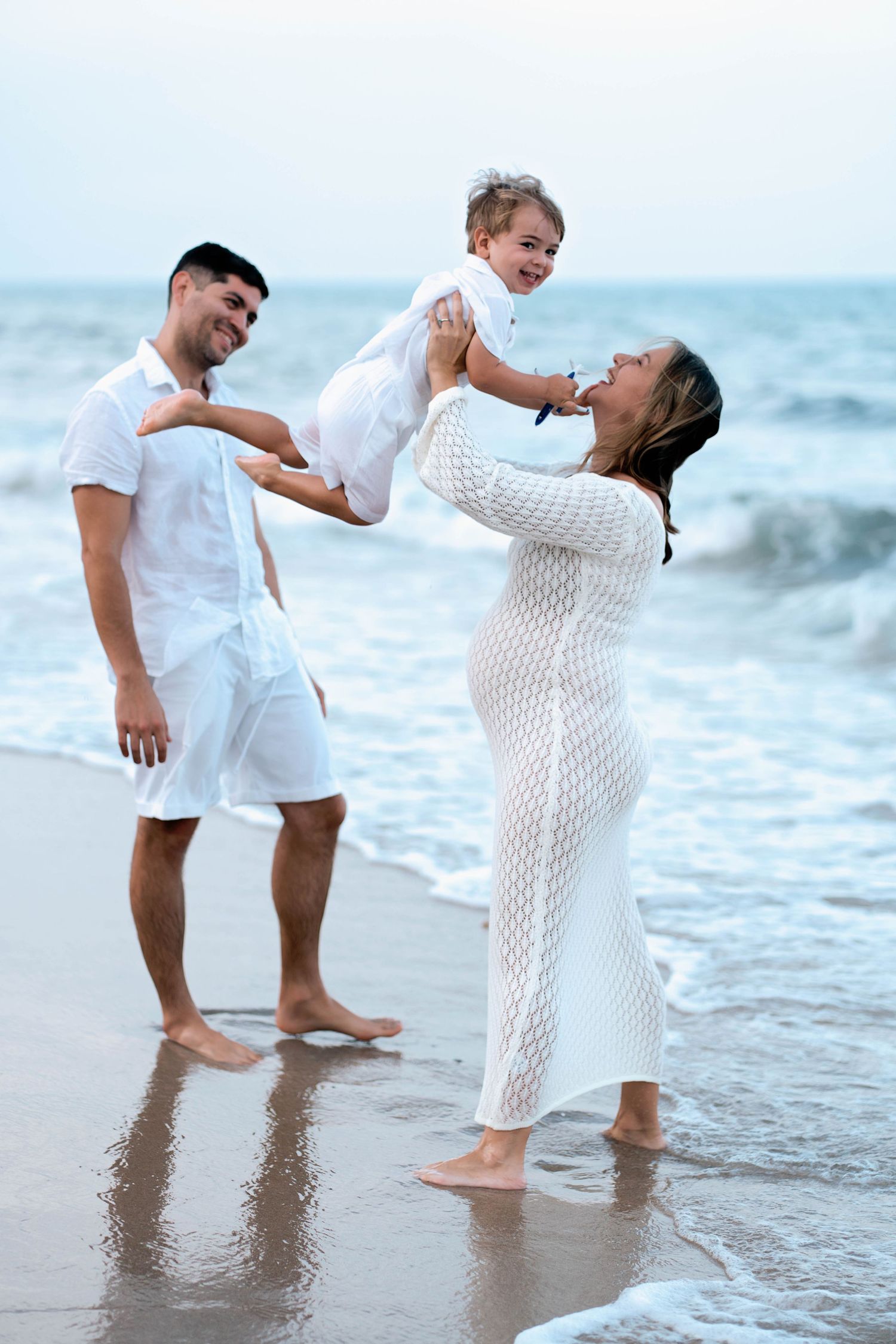 Family playing together at the beach edge in white outfits.
