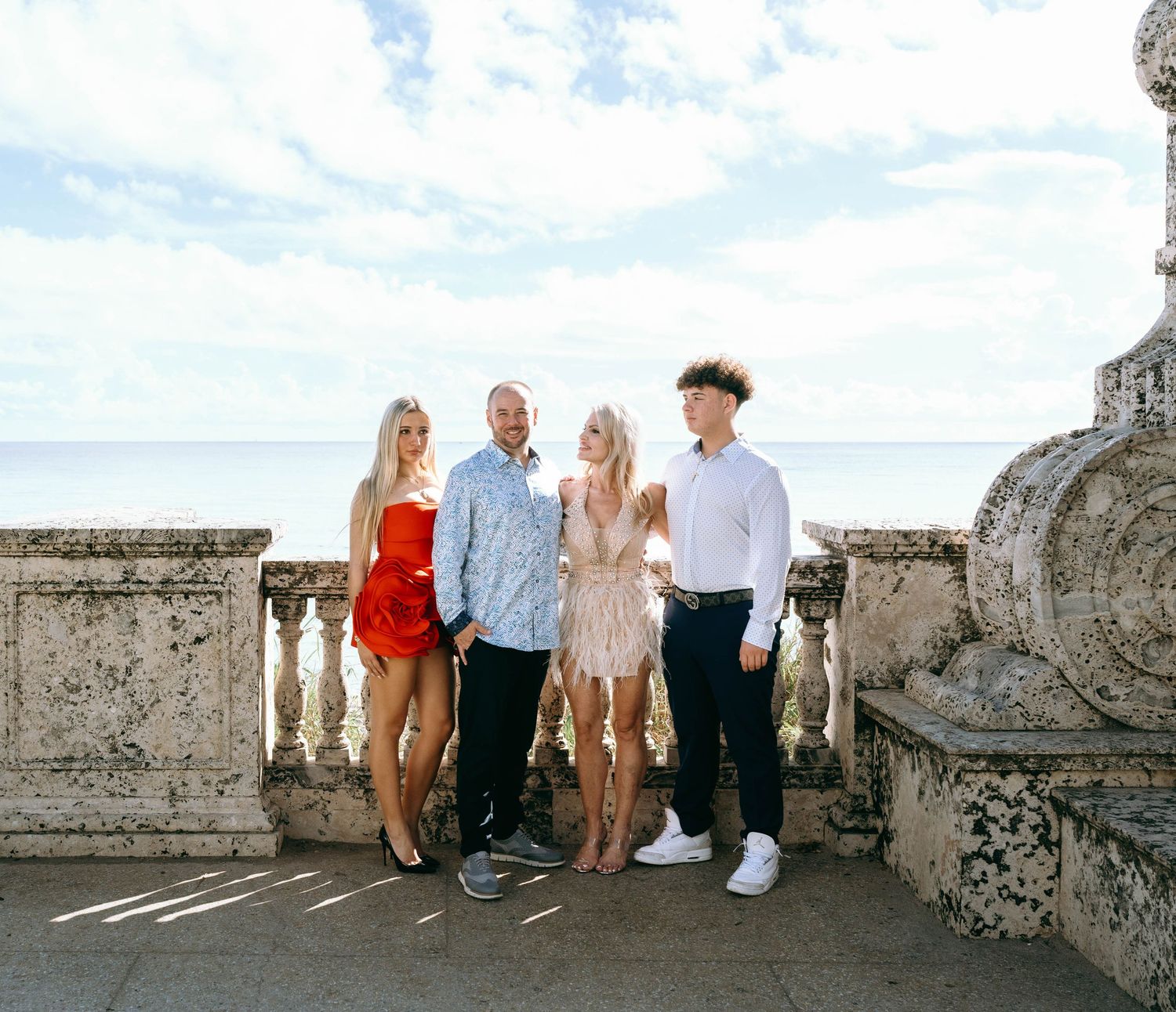 Family photoshoot on a sunny day at a historic stone balcony with palm trees in the background.