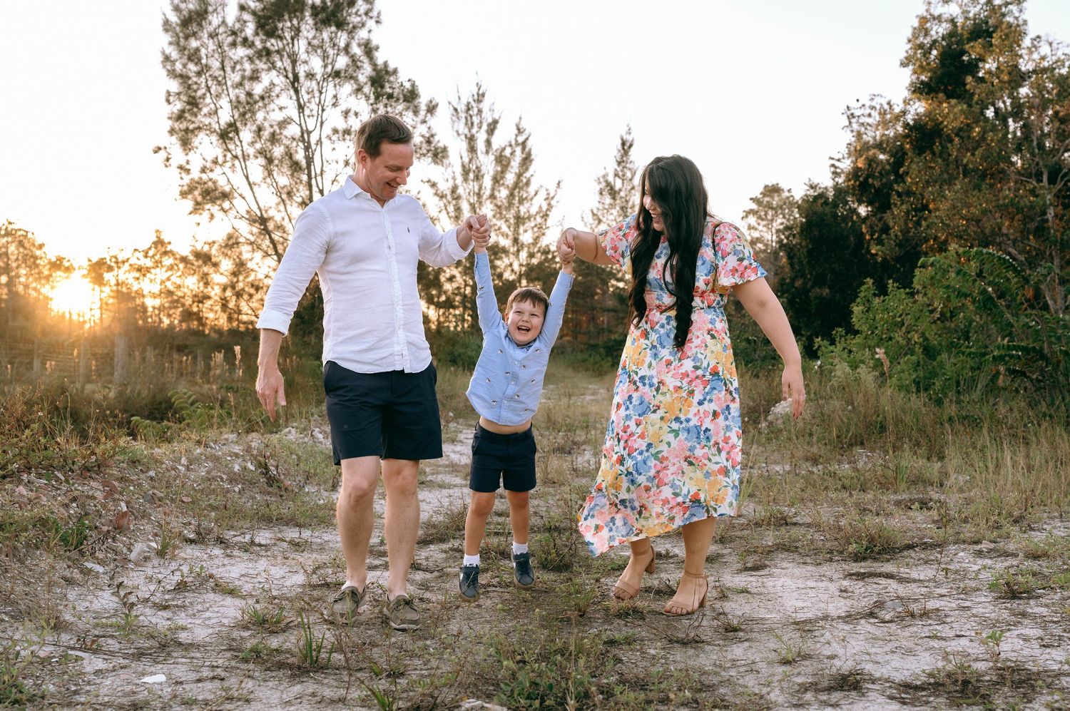 A family shares joyful moments together during a sunset photoshoot in a natural outdoor setting.