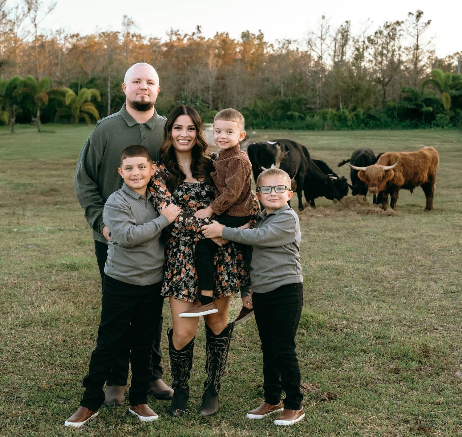 Family of five posing outdoors in a green field with longhorn cattle in the background during golden hour at Colt Farms in Boynton Beach FL.