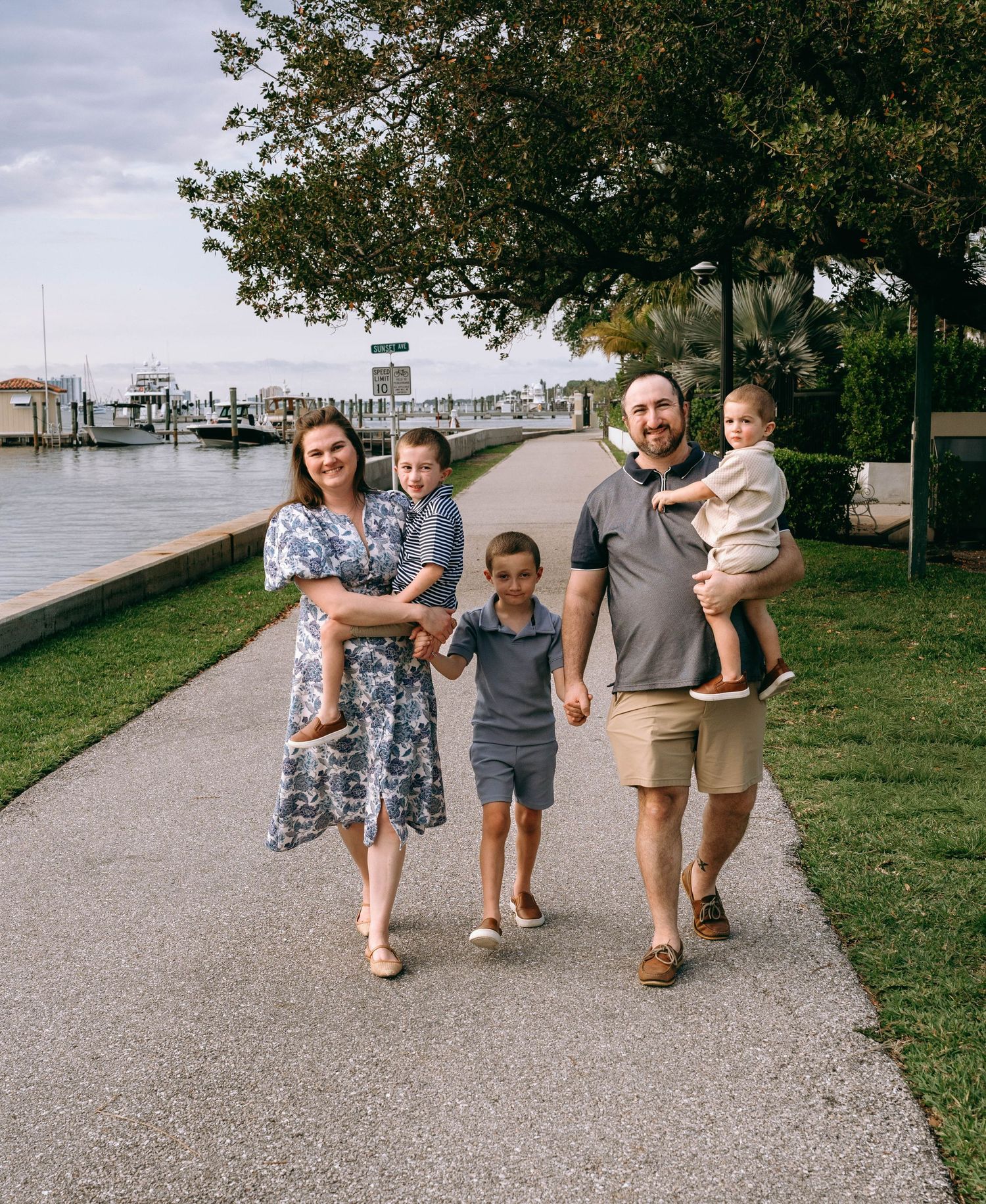 Happy family of five walking along waterfront path near marina on a cloudy day.  Family photos at Bradley Park Palm Beach, FL