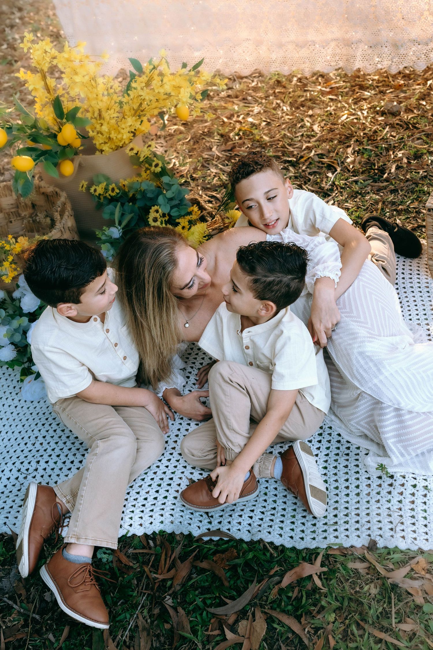 A family in white and beige outfits shares playful moments together while sitting on a blanket outdoors in autumn.