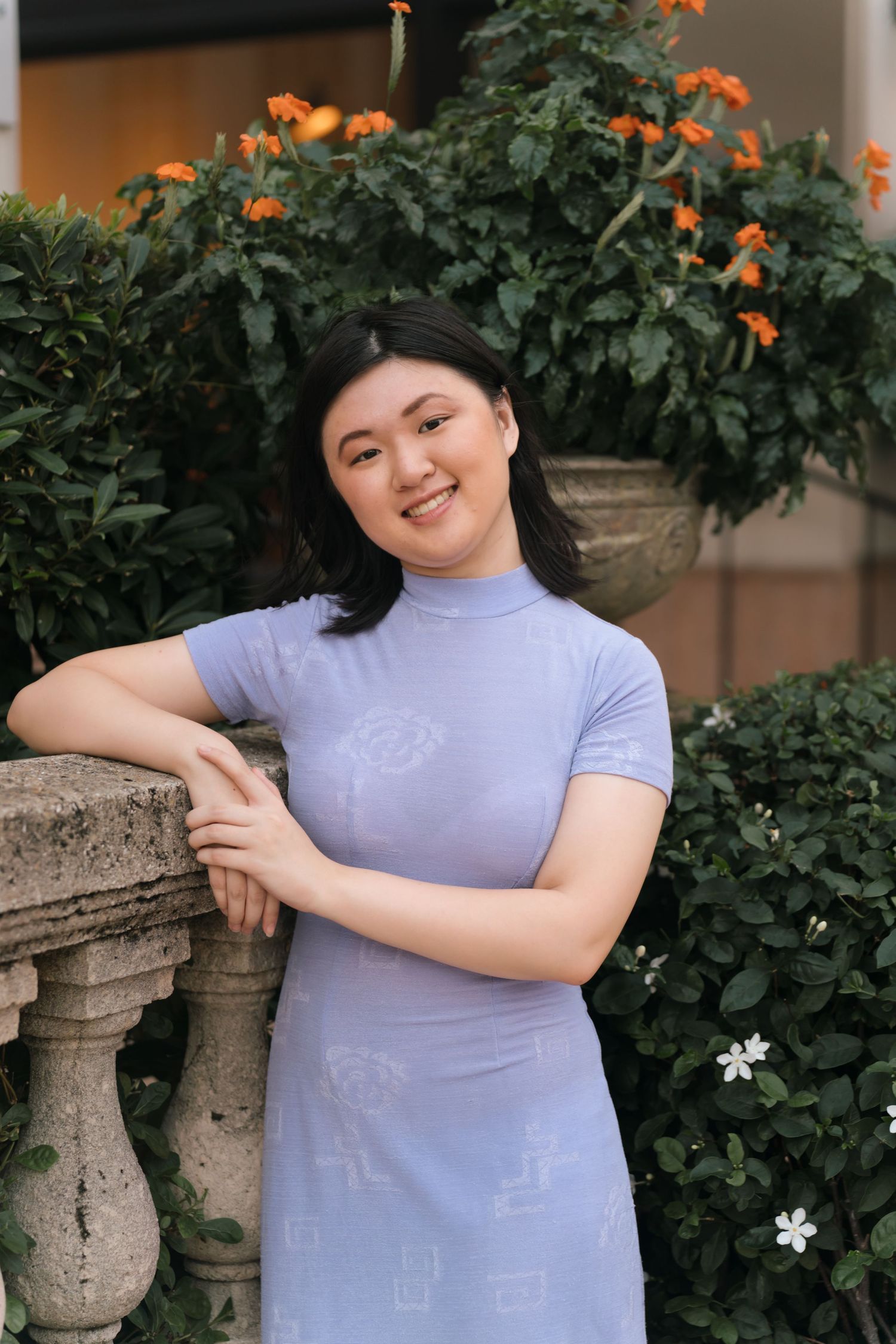 A lavender fitted dress photographed against orange flowers and stone architecture.