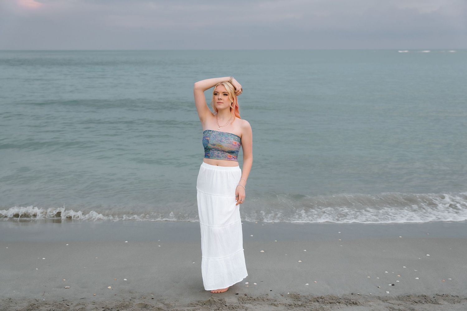 A beach photoshoot featuring a grey top and white maxi skirt against ocean waves.