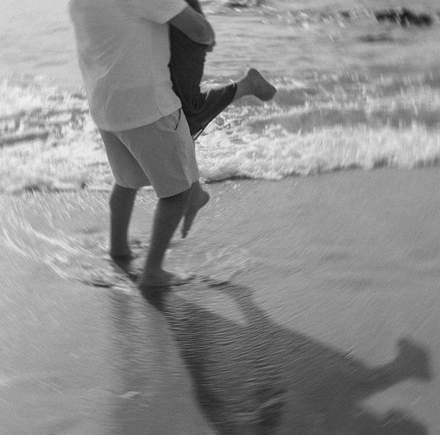 Black and white photo of feet walking through gentle ocean waves.
