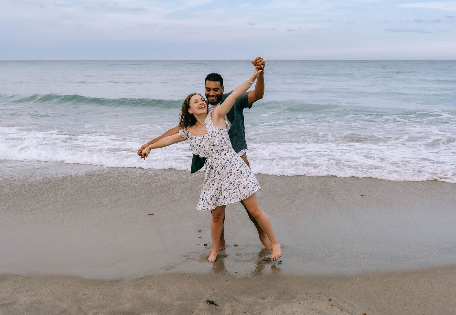 Happy couple dancing barefoot on a sandy beach with ocean waves in the background on Worth Avenue Palm beach.
