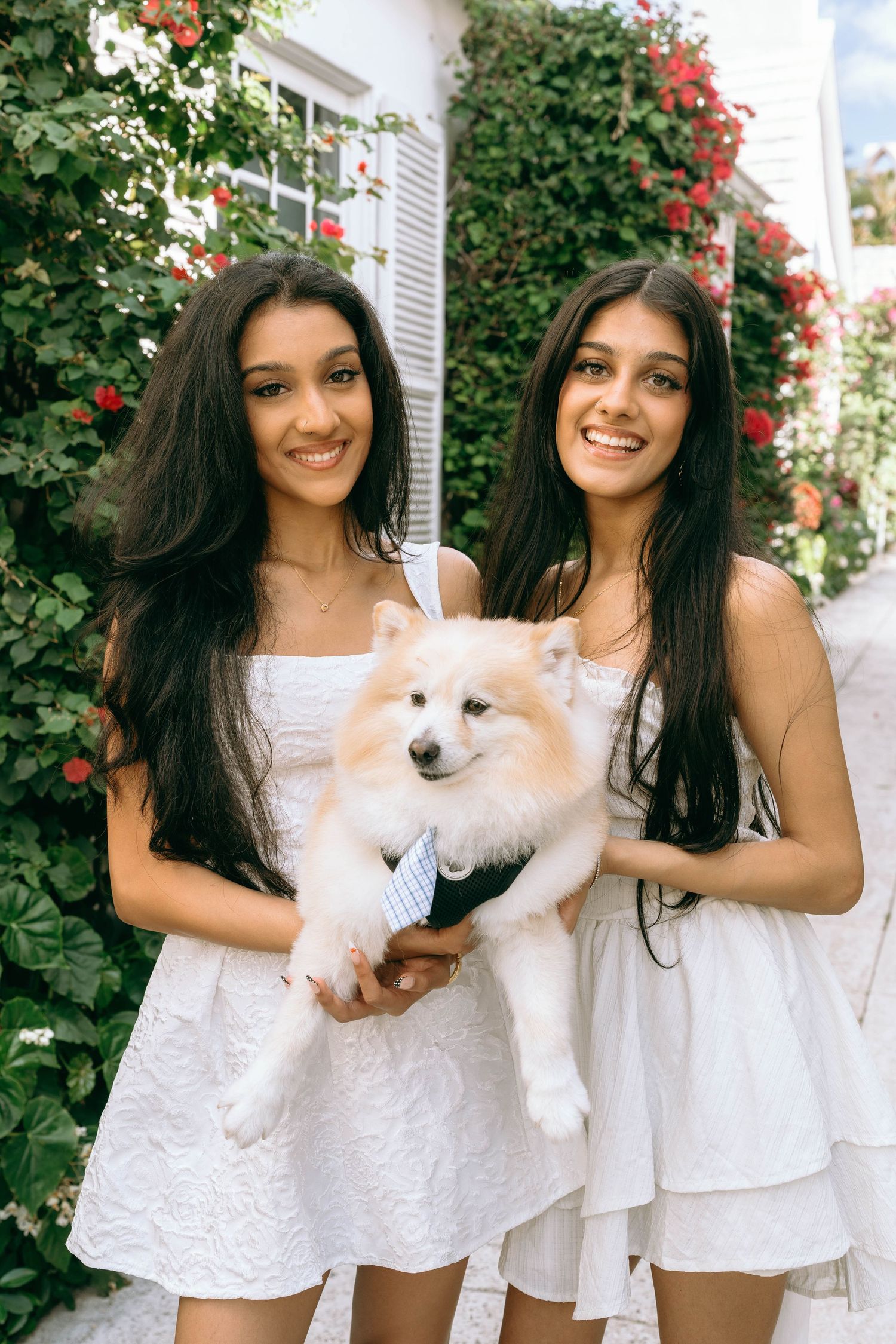 Two young women in white dresses holding a fluffy white Pomeranian dog outdoors on Worth Avenue Palm beach.
