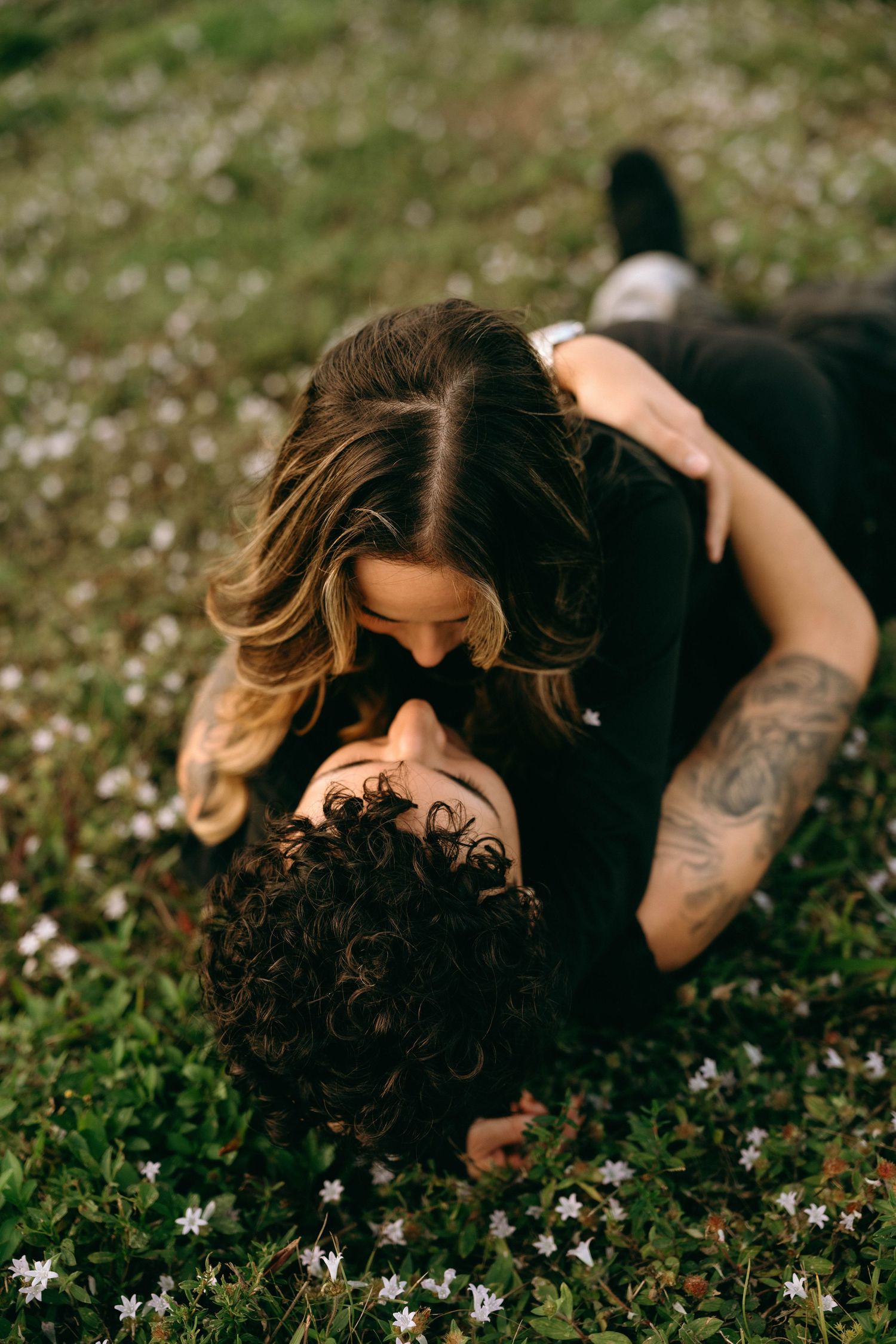 Couple lying together among wildflowers in grassy field.