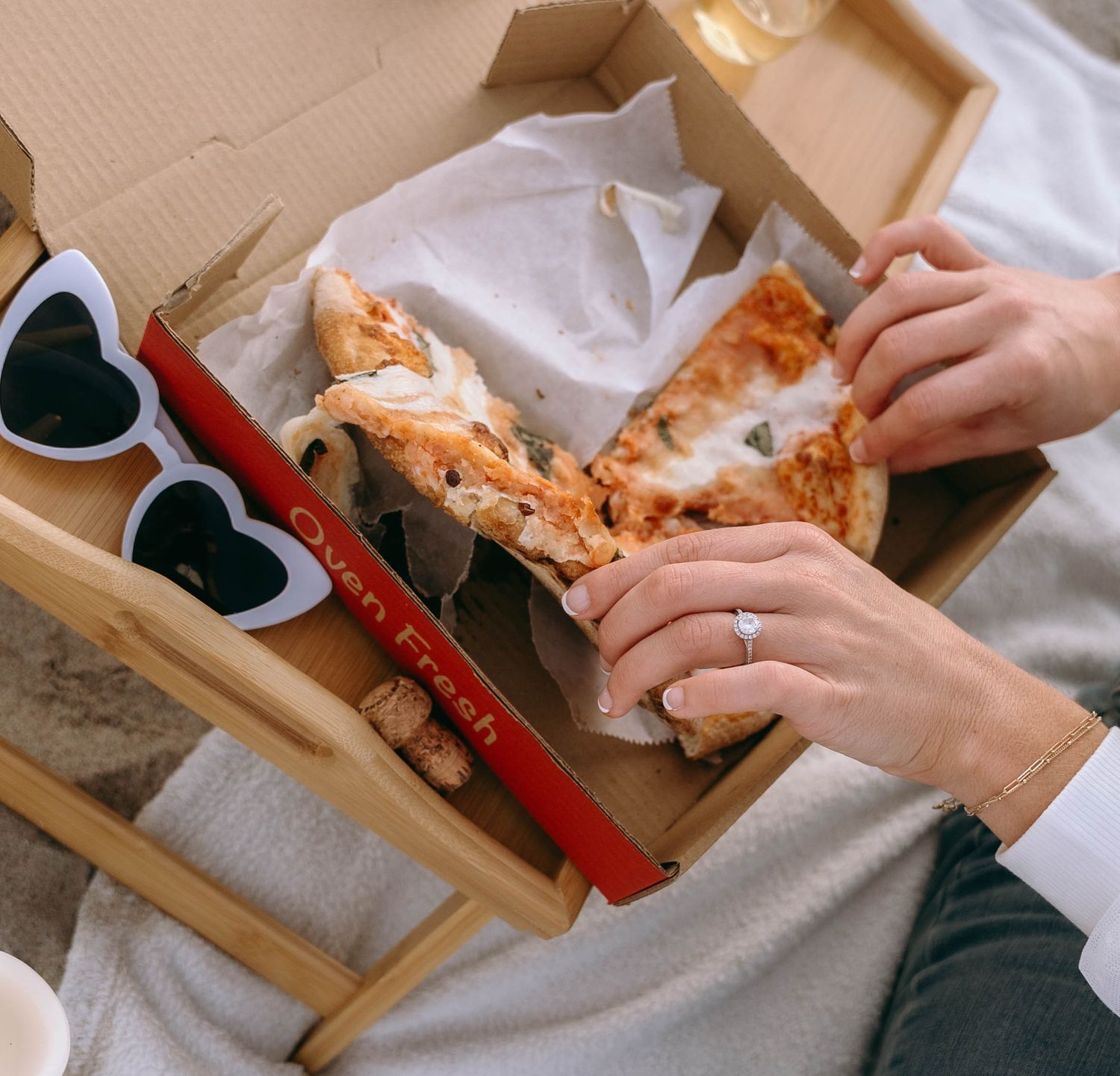 A pizza box with heart-shaped sunglasses and hands reaching for a slice.