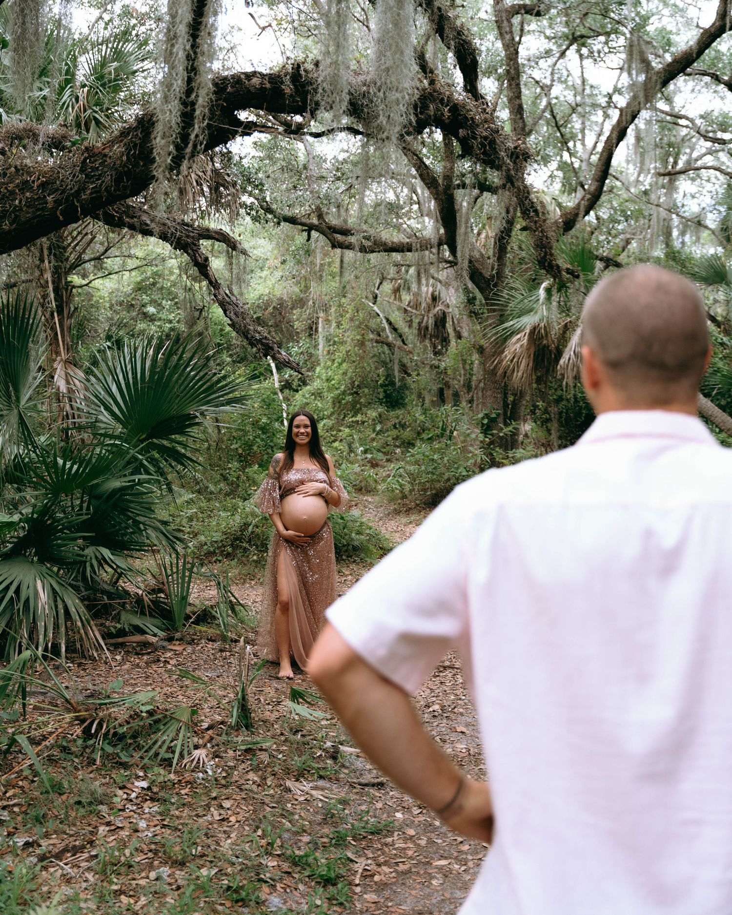 Romantic proposal moment captured in wooded area with Spanish moss hanging from trees.