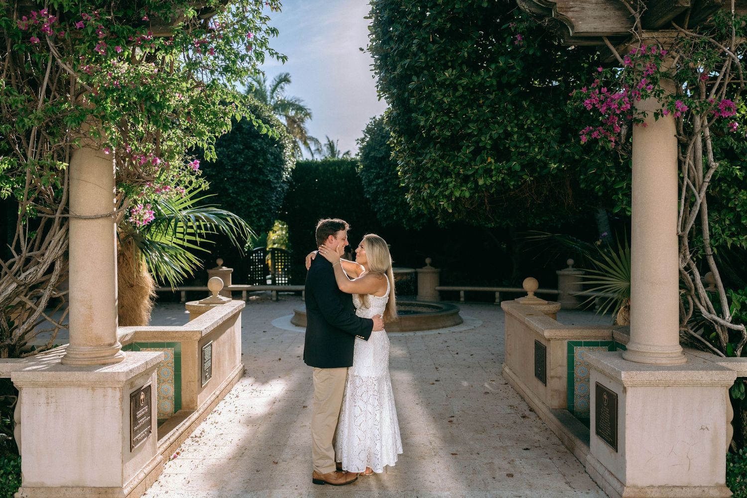Couple embracing and kissing in elegant garden walkway surrounded by lush tropical greenery.