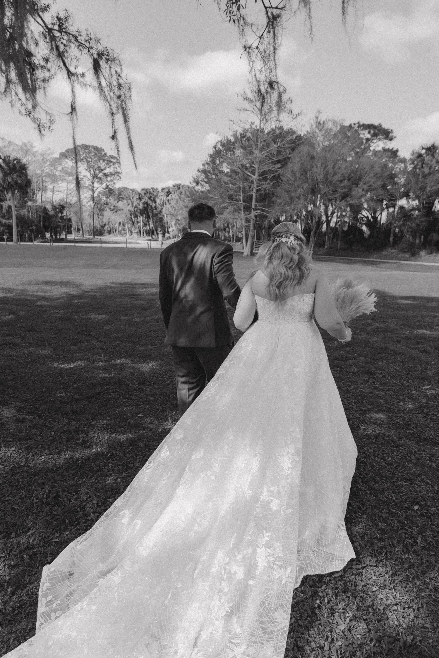 Black and white photo of couple walking through scenic outdoor wedding venue.