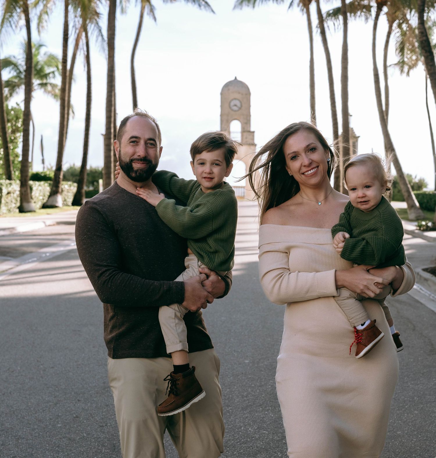 A family poses together on a palm-lined path with a church tower visible in the background.