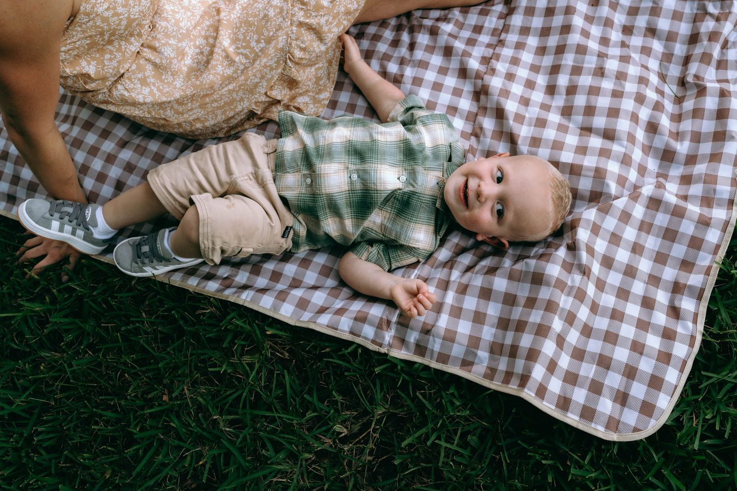 Baby lying on checkered blanket during outdoor photoshoot.