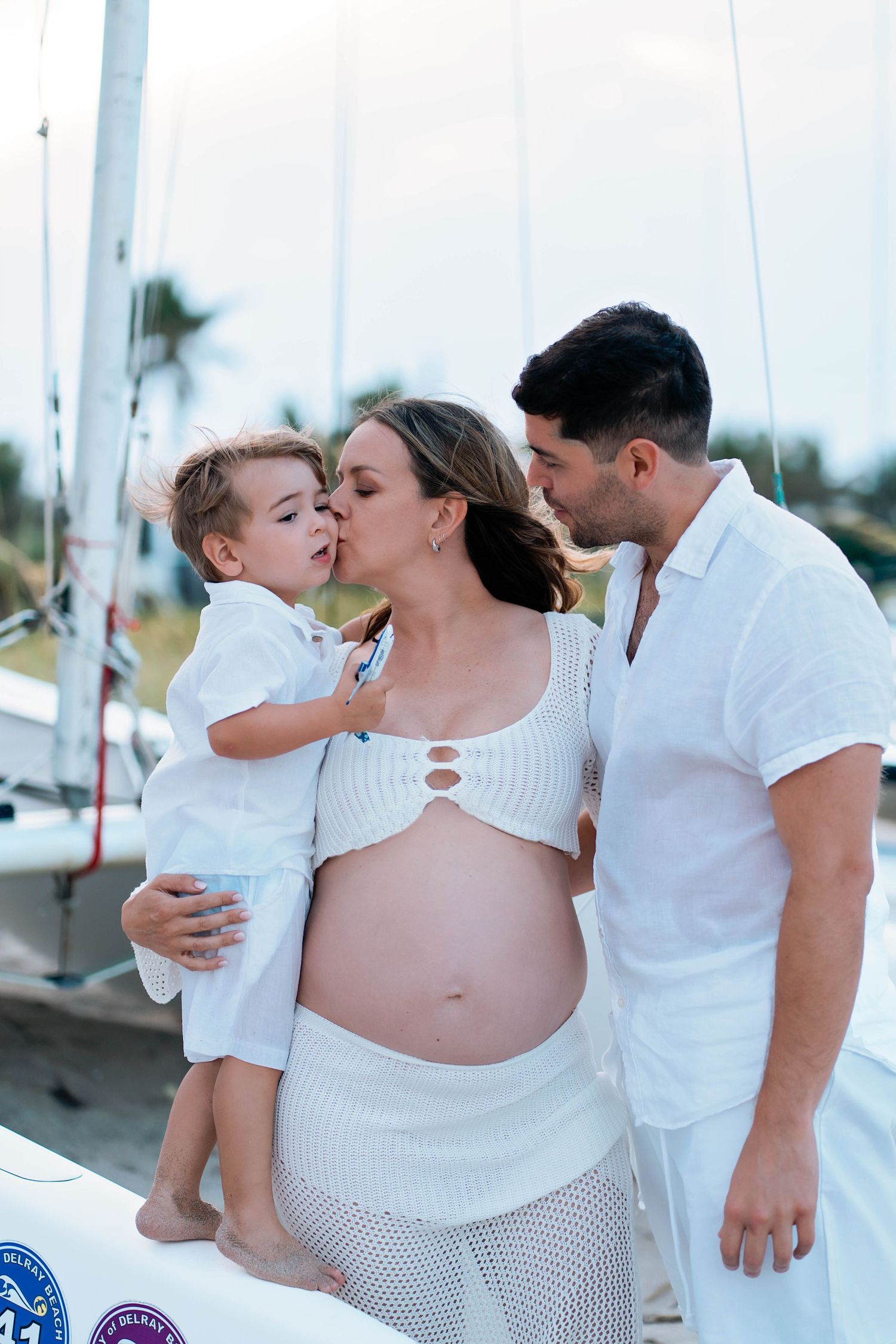 Family maternity photoshoot on beach in all-white attire.