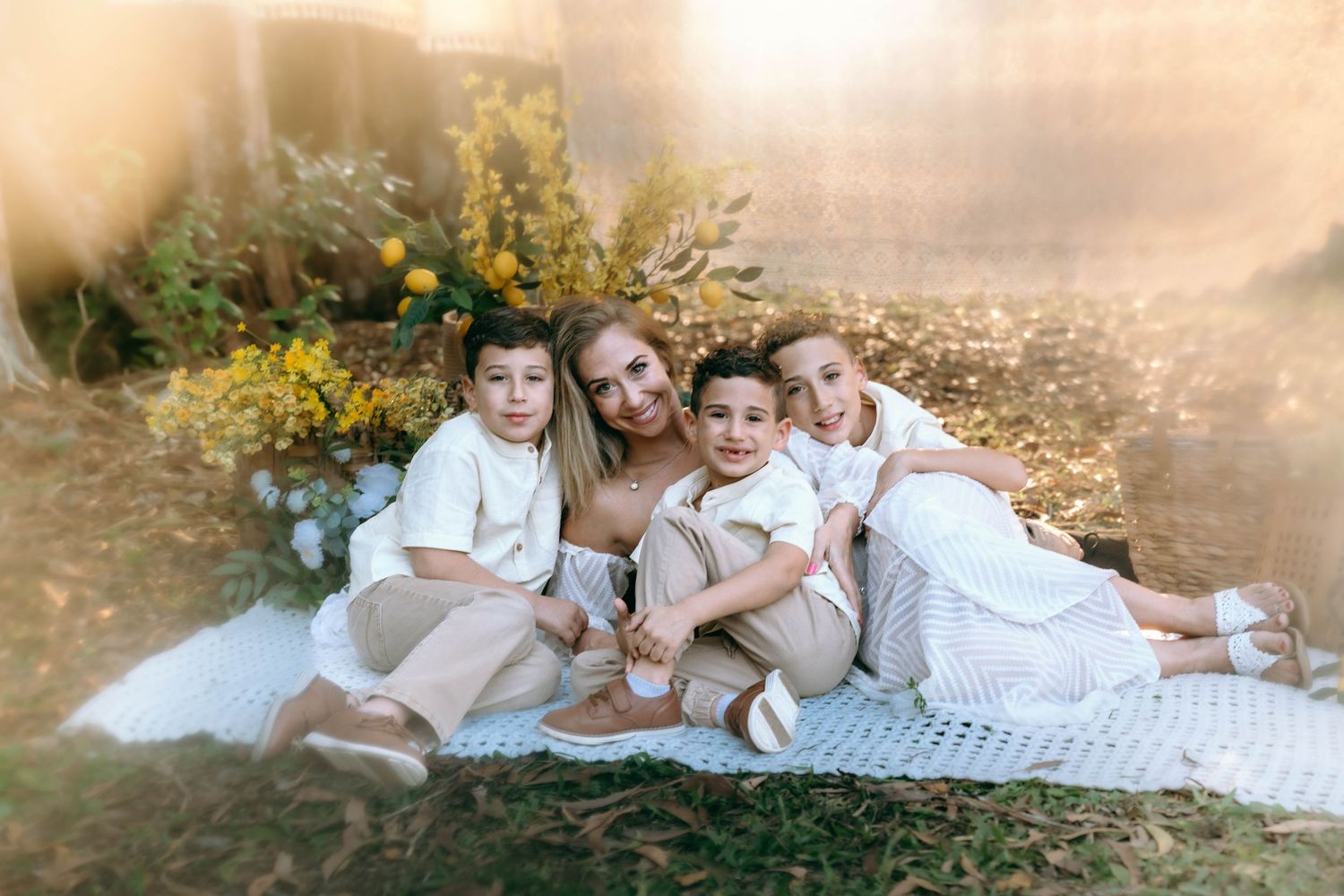 A dreamy outdoor portrait of a group in white dresses sitting together on a blanket with yellow flowers in the background.
