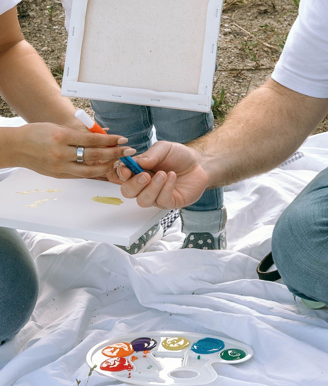 Two people painting on a canvas outdoors with colorful paint palette on a white cloth.