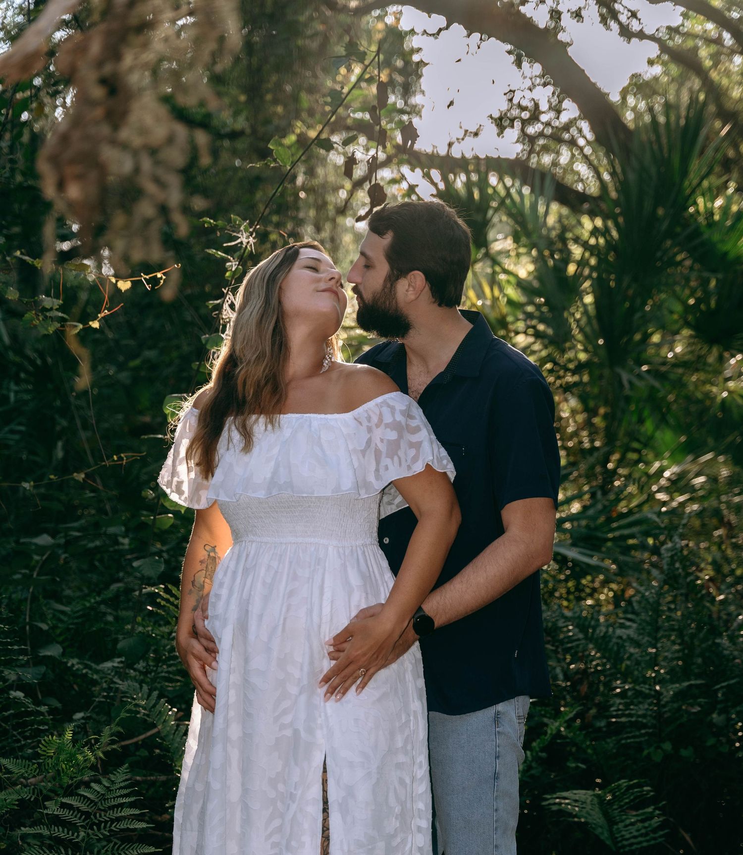 Romantic moment captured in a wooded area with sunlight filtering through the trees.