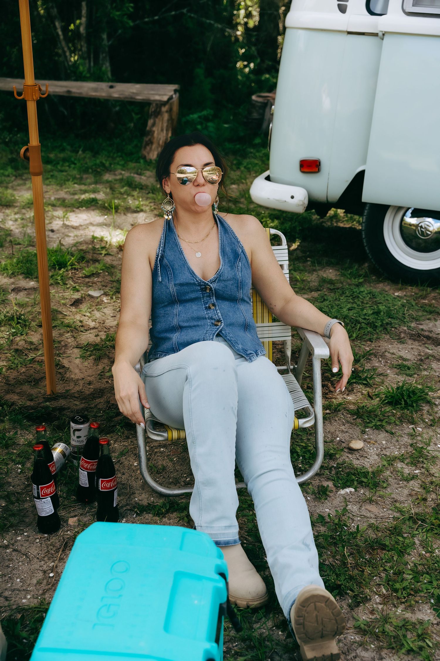 Person sitting in camping chair next to vintage van with turquoise cooler.